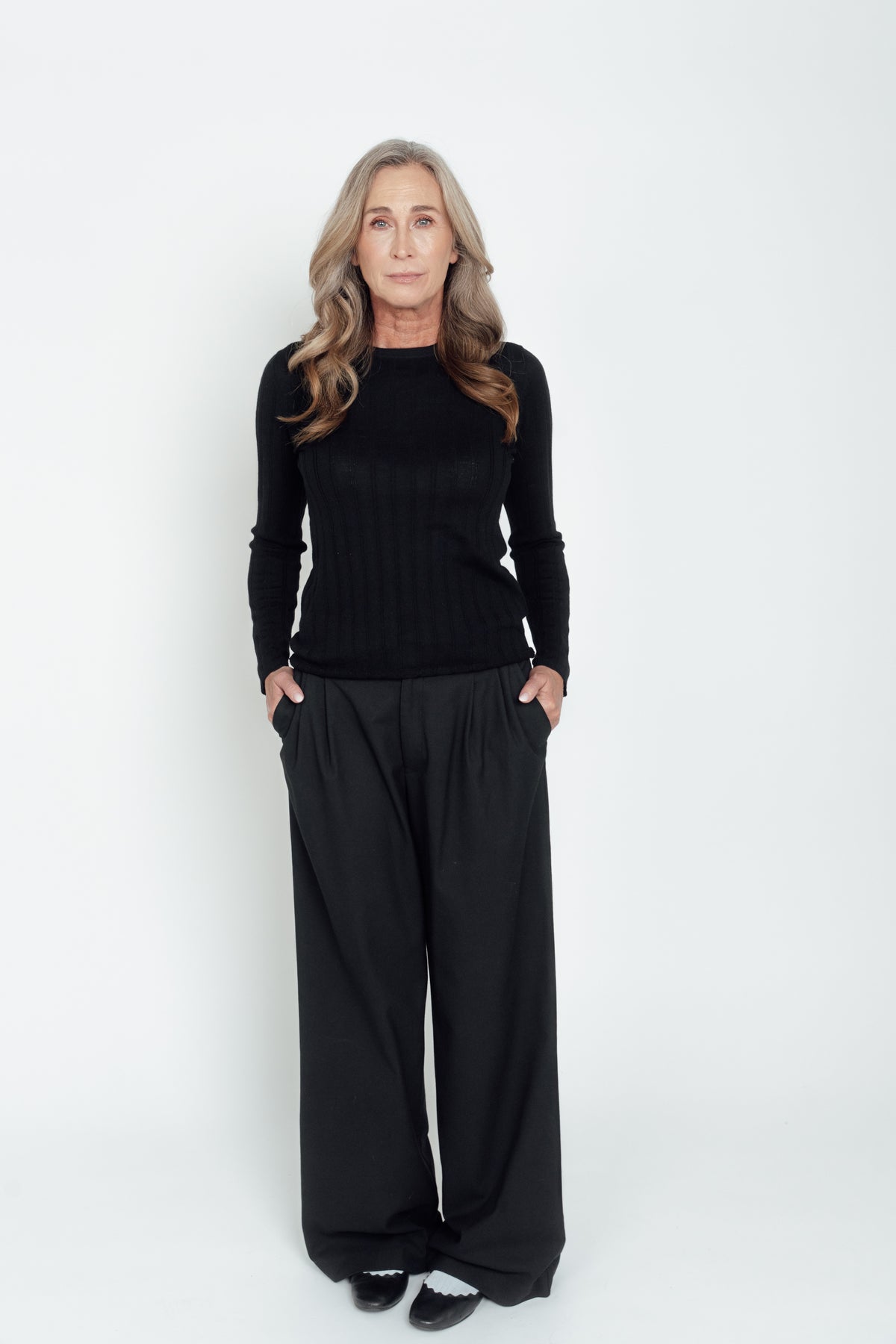 Black Ivy Merino Top worn with wide-leg trousers, with the model's hands in her pockets.