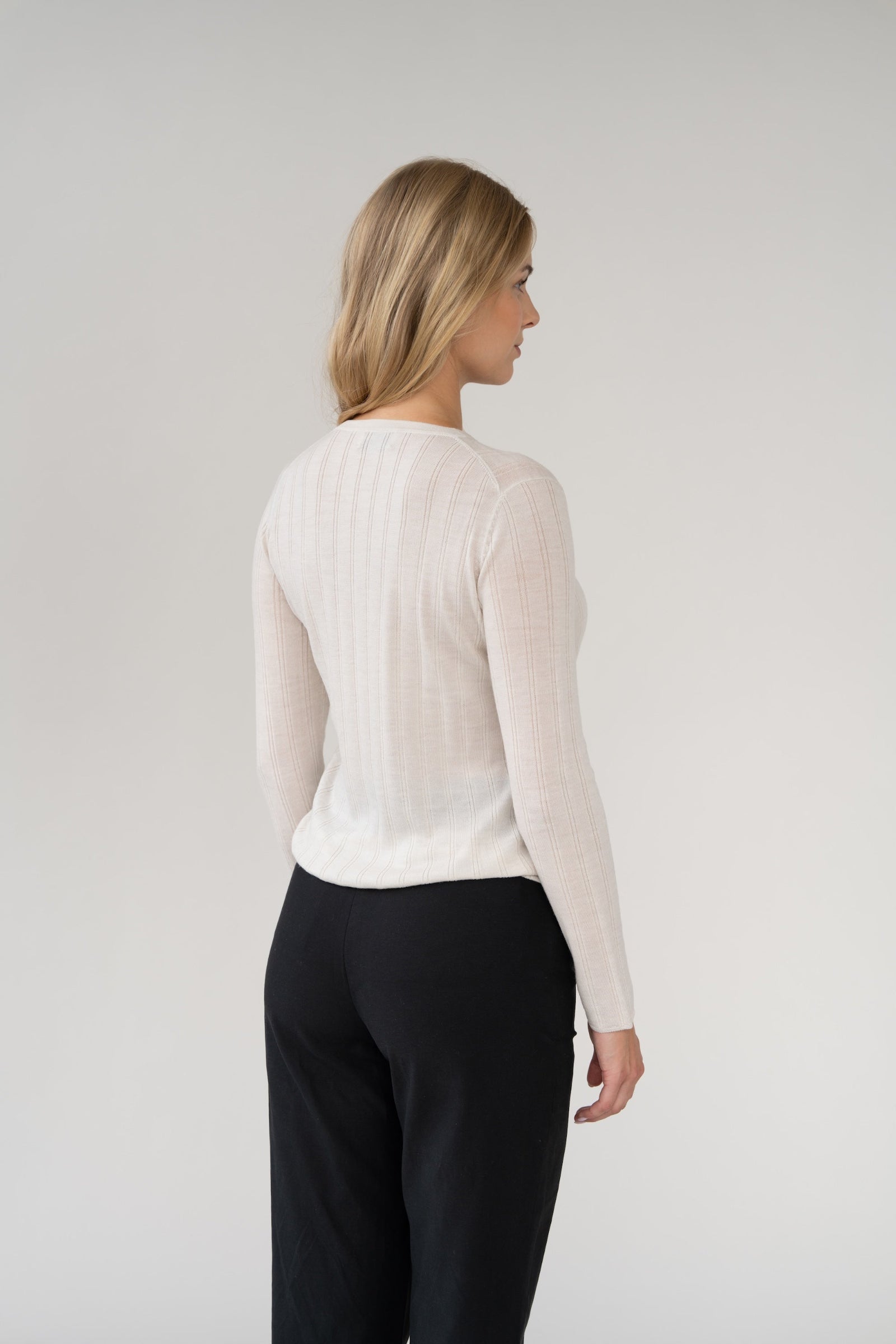 Woman wearing a white ribbed long-sleeve top and black pants against a plain background