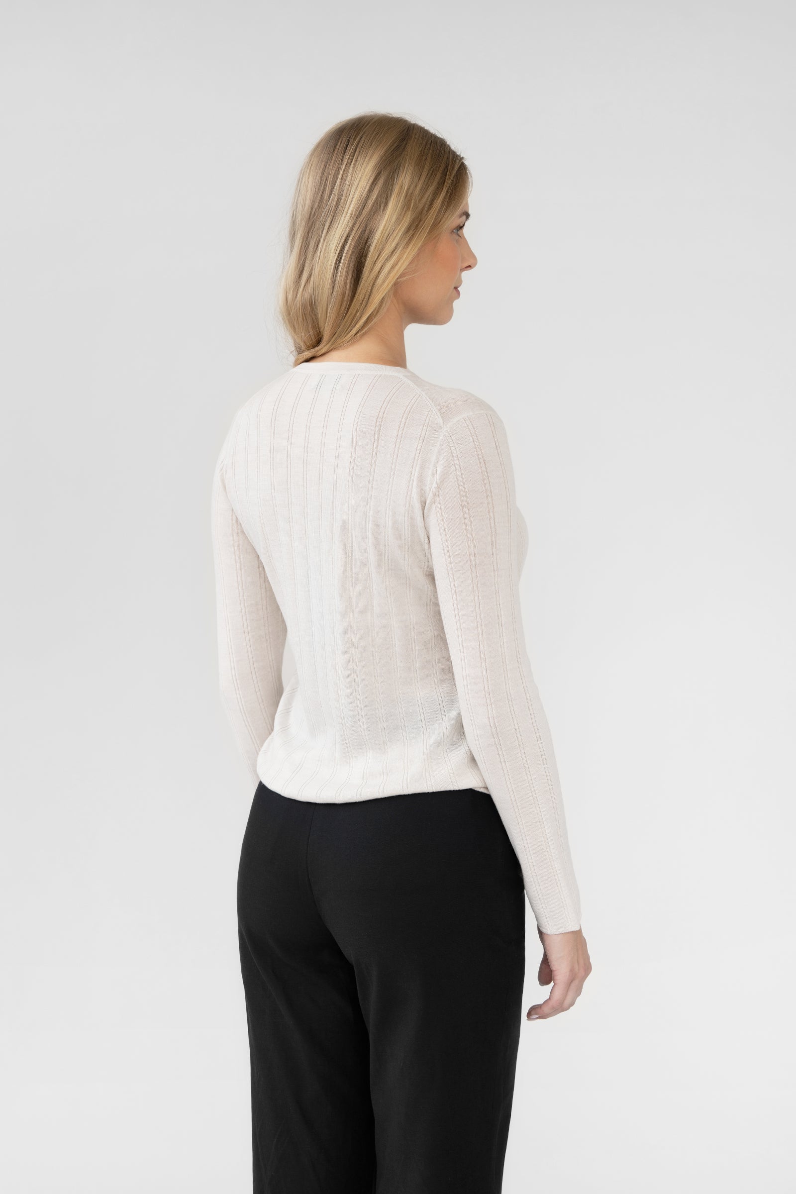 Woman wearing a white ribbed long-sleeve top and black pants against a plain background