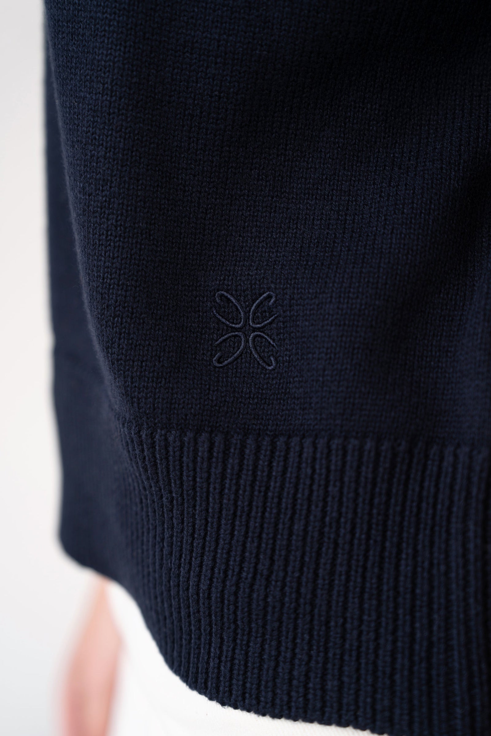 Close-up of ribbed hem with tone-on-tone embroidered logo on short-sleeve knit top, navy, studio.