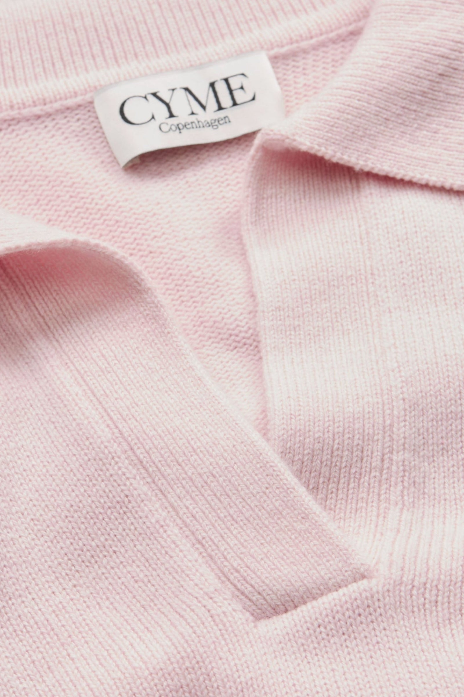 A close-up of the collar and neckline of a light pink polo-style knit jumper, featuring a "CYME Copenhagen" label.