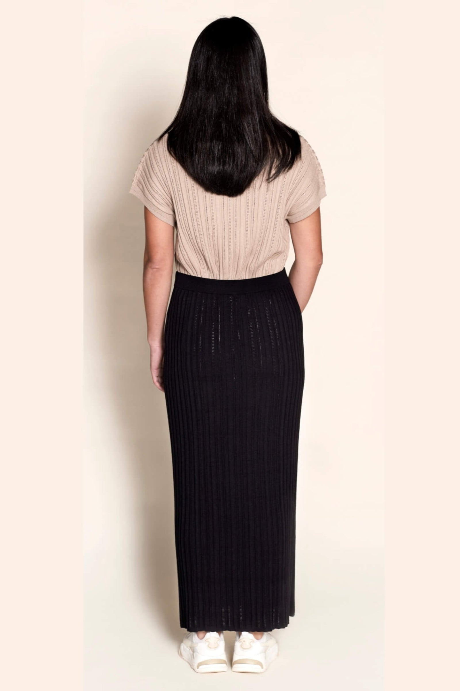 Back view of a model in Cyme Copenhagen attire, pairing a taupe ribbed knit top with a black knit skirt, highlighting the brand's fusion of comfort and Danish designer fashion in sustainable women's clothing.