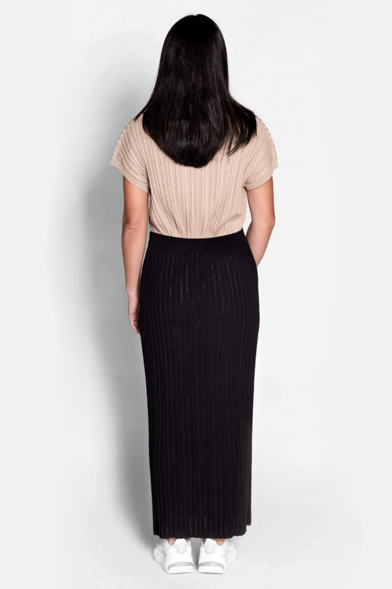Back view of a model in Cyme Copenhagen attire, pairing a taupe ribbed knit top with a black knit skirt, highlighting the brand's fusion of comfort and Danish designer fashion in sustainable women's clothing.