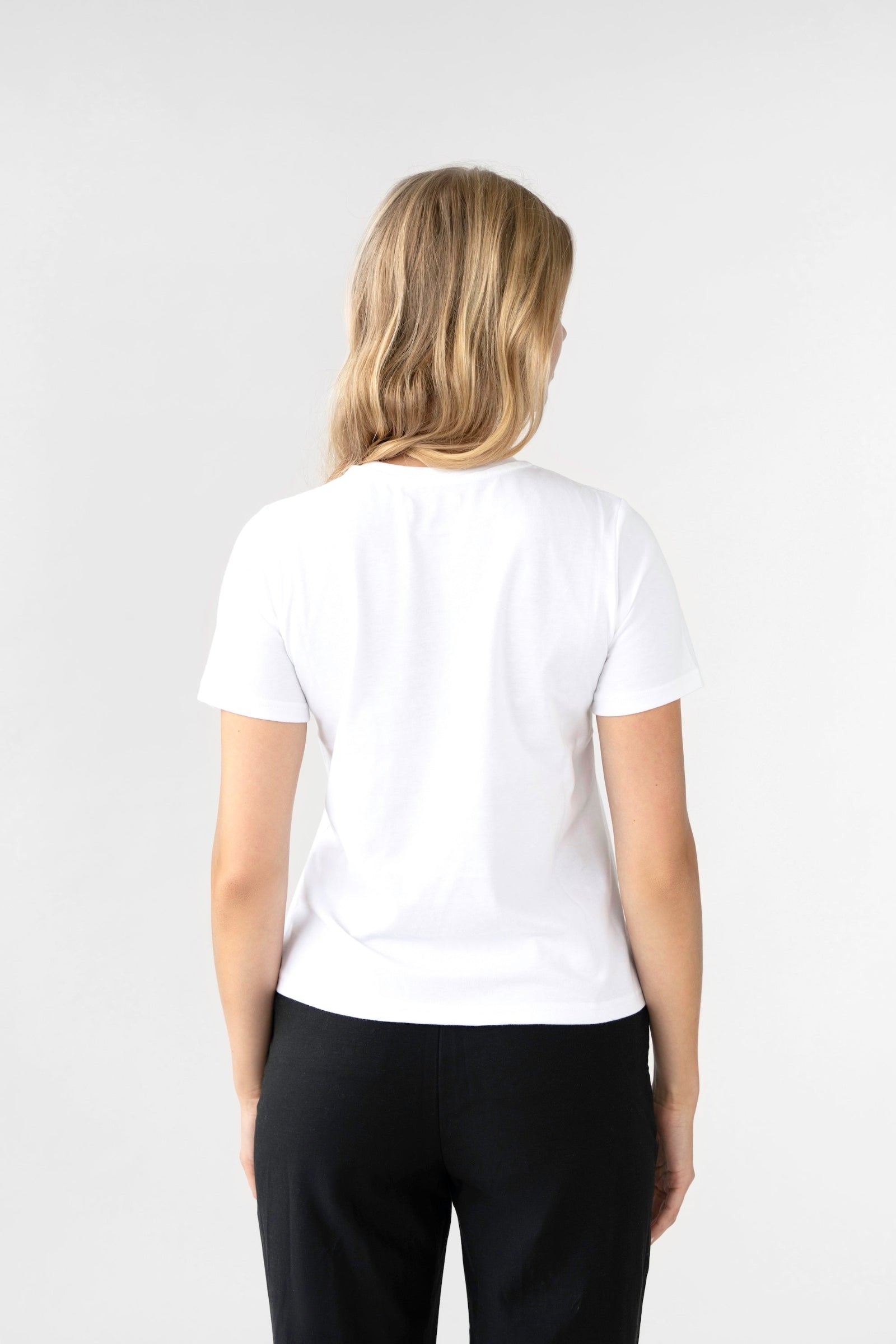 Person wearing a white t-shirt and black pants on a plain background