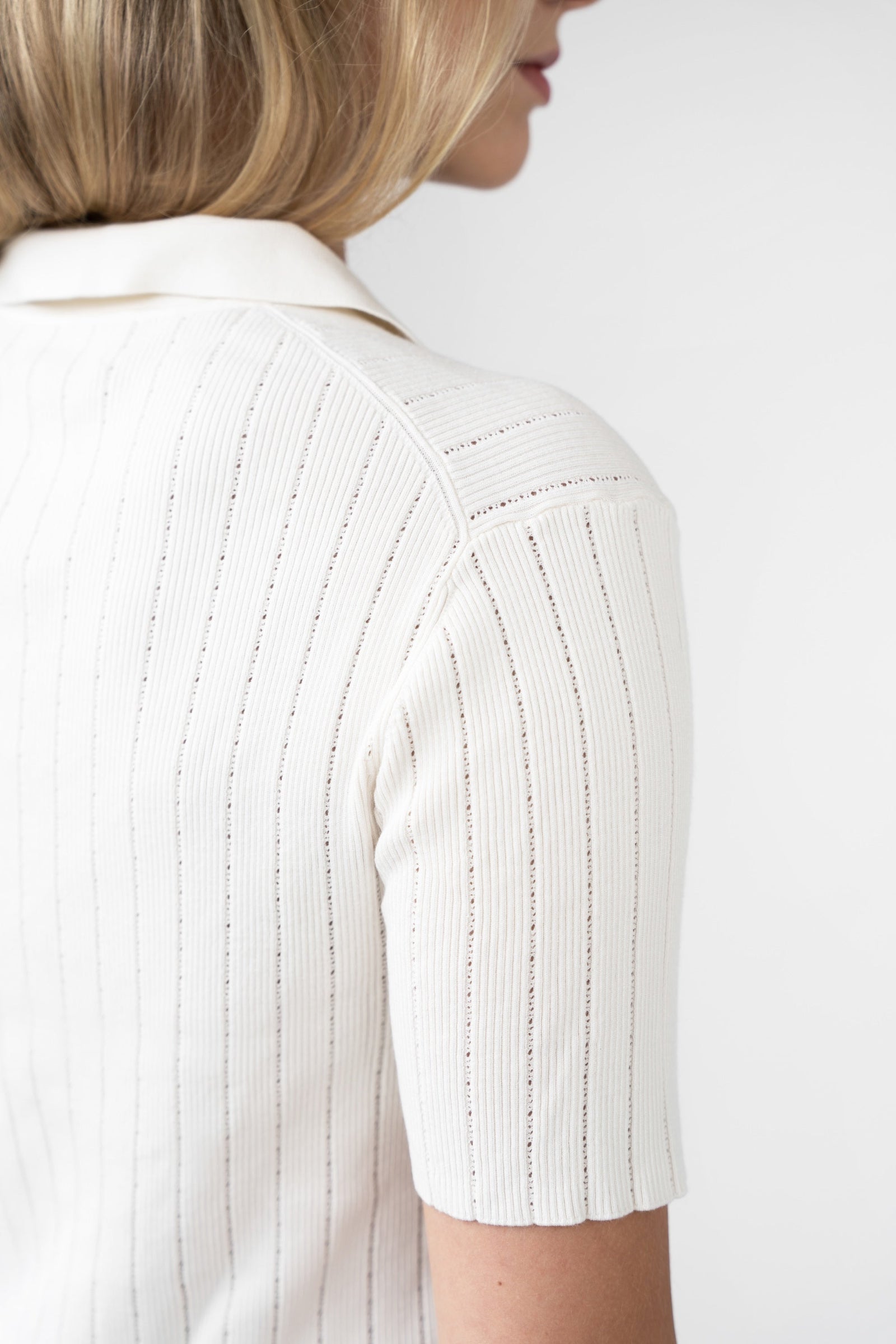 Close-up of a person wearing a white ribbed knit top on a plain background