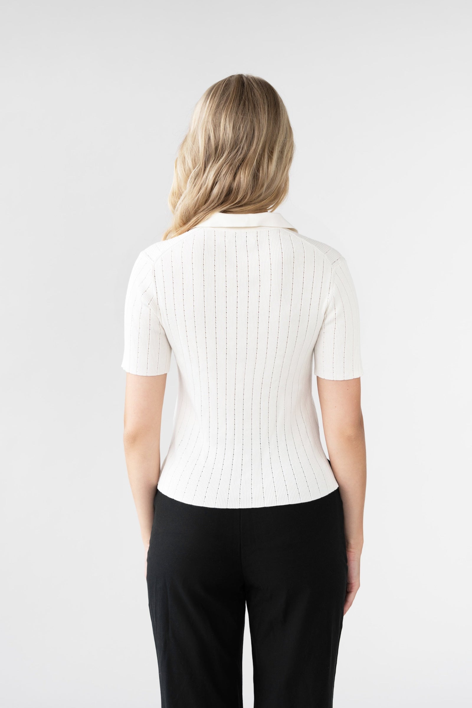 Person wearing a white ribbed knit top and black pants on a light gray background