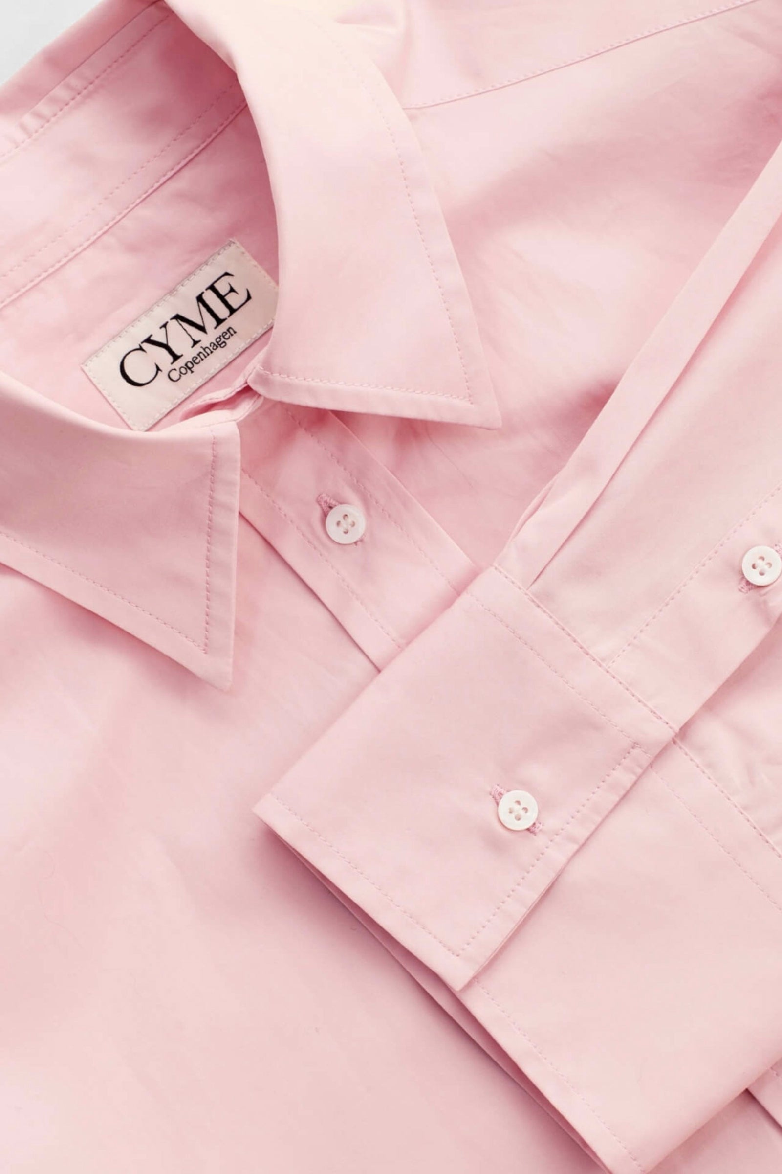 Detail of a delicate pink supima cotton shirt by Cyme Copenhagen, showcasing the brand's label, precision stitching, and commitment to sustainable fashion materials, encapsulating the ethos of a top Danish designer in women's clothing.