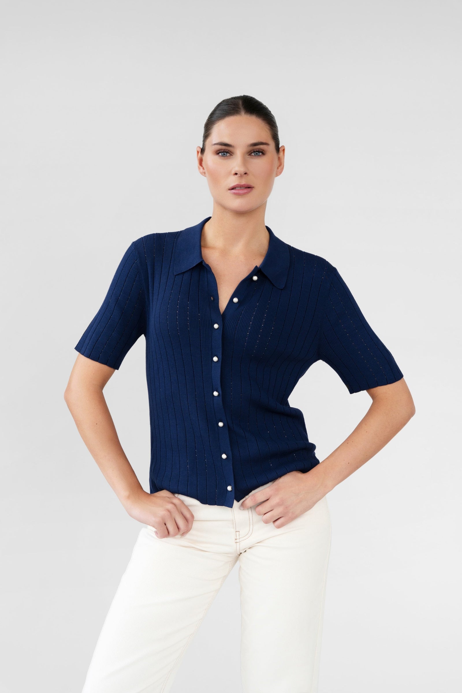 Woman wearing a navy blue short-sleeve shirt and white pants on a light gray background