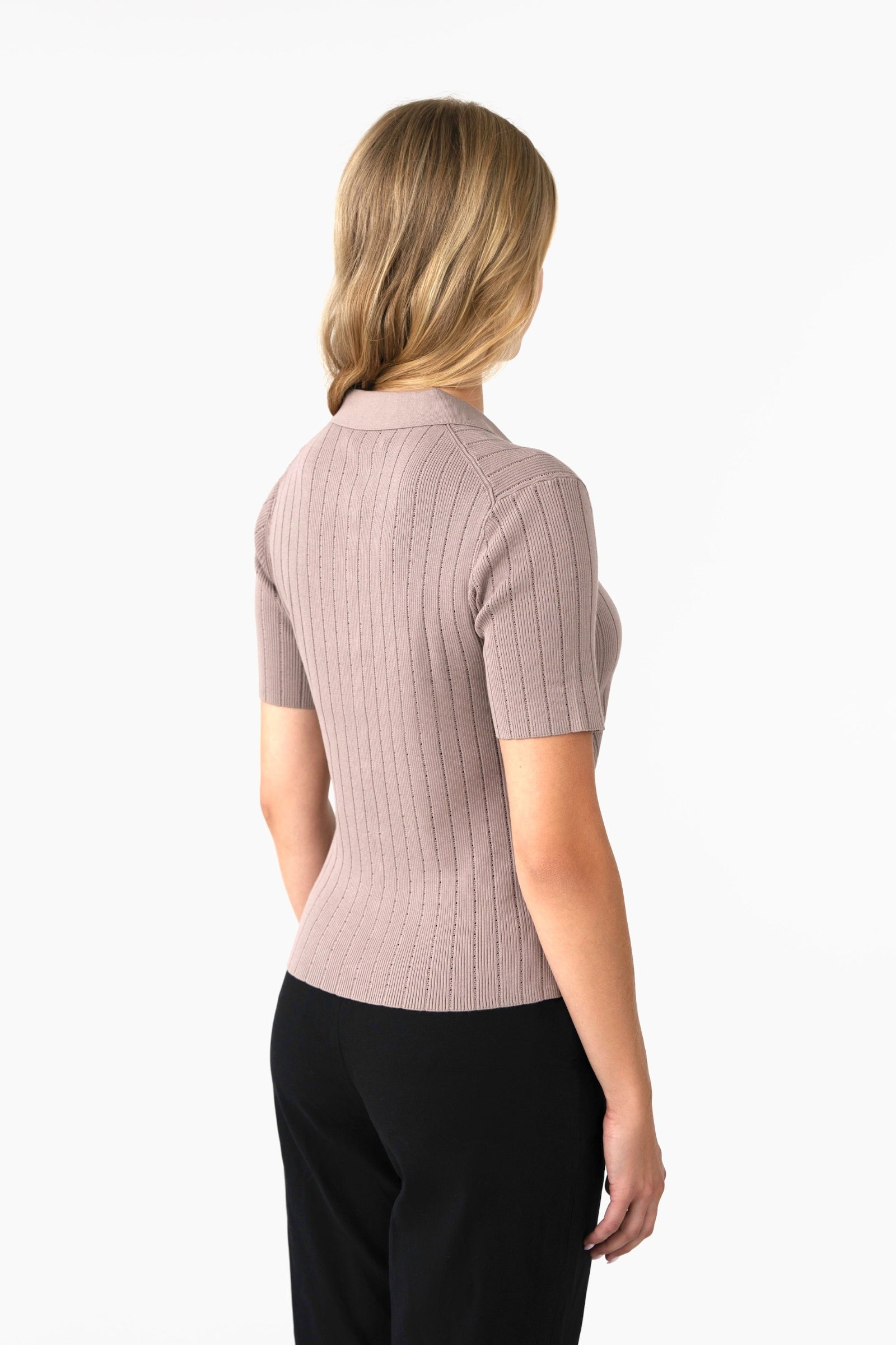 Woman wearing a beige ribbed short-sleeve top and black pants on a white background