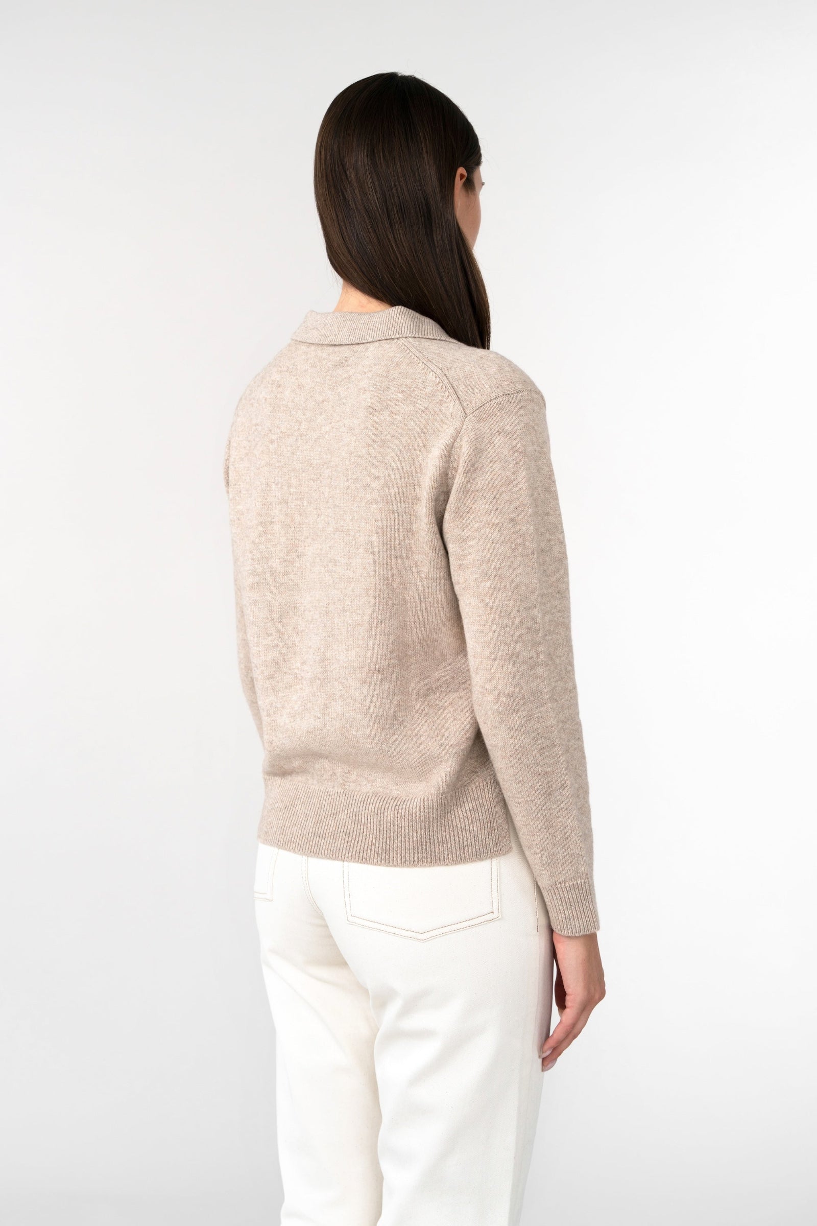Woman wearing a beige sweater and white pants on a white background