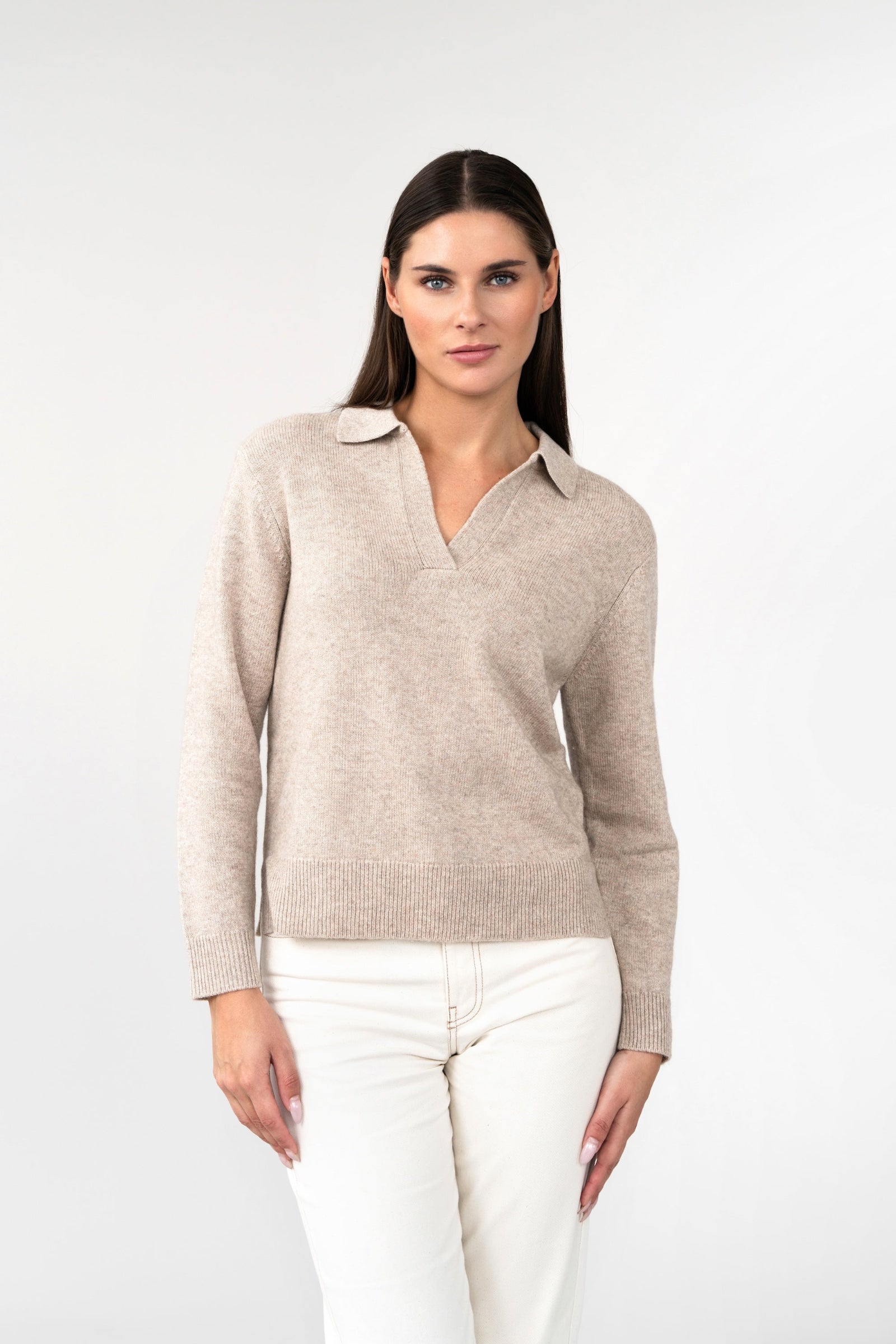 Woman wearing a beige sweater and white pants on a white background