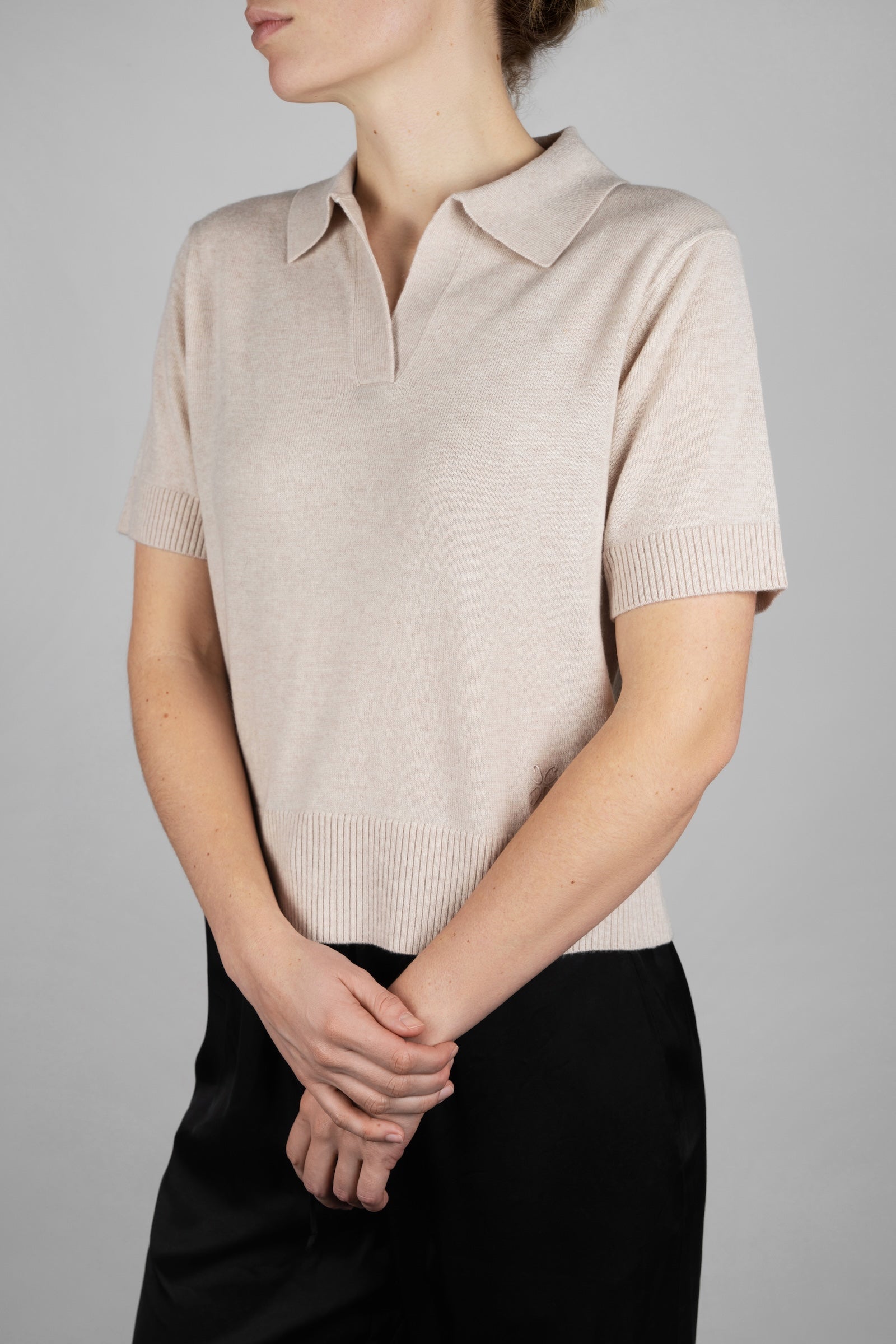 Person wearing a beige short-sleeve knit polo shirt against a gray background