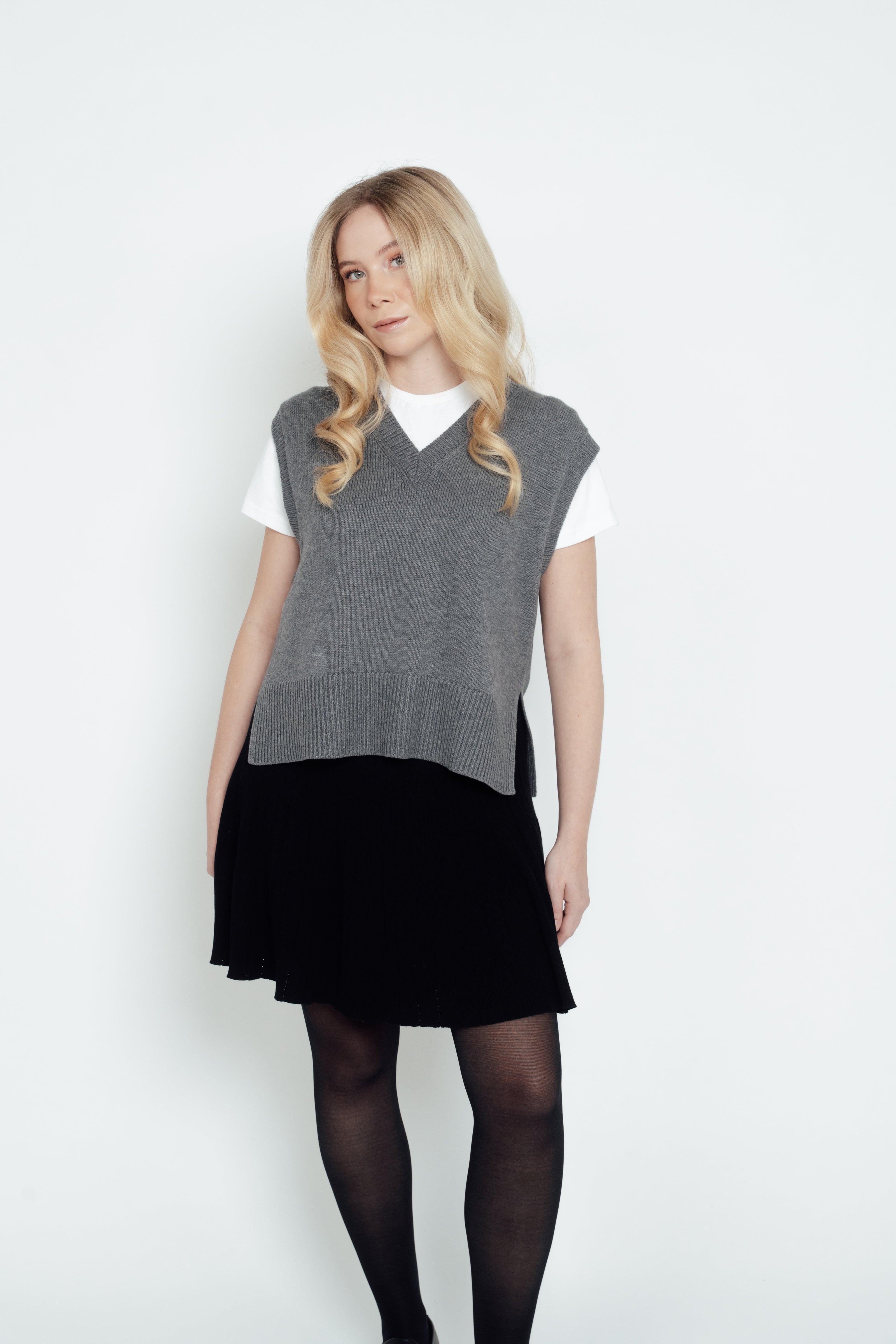 A woman models the grey CYME Merino V-Neck Vest over a white T-shirt with a black skirt and loafers.
