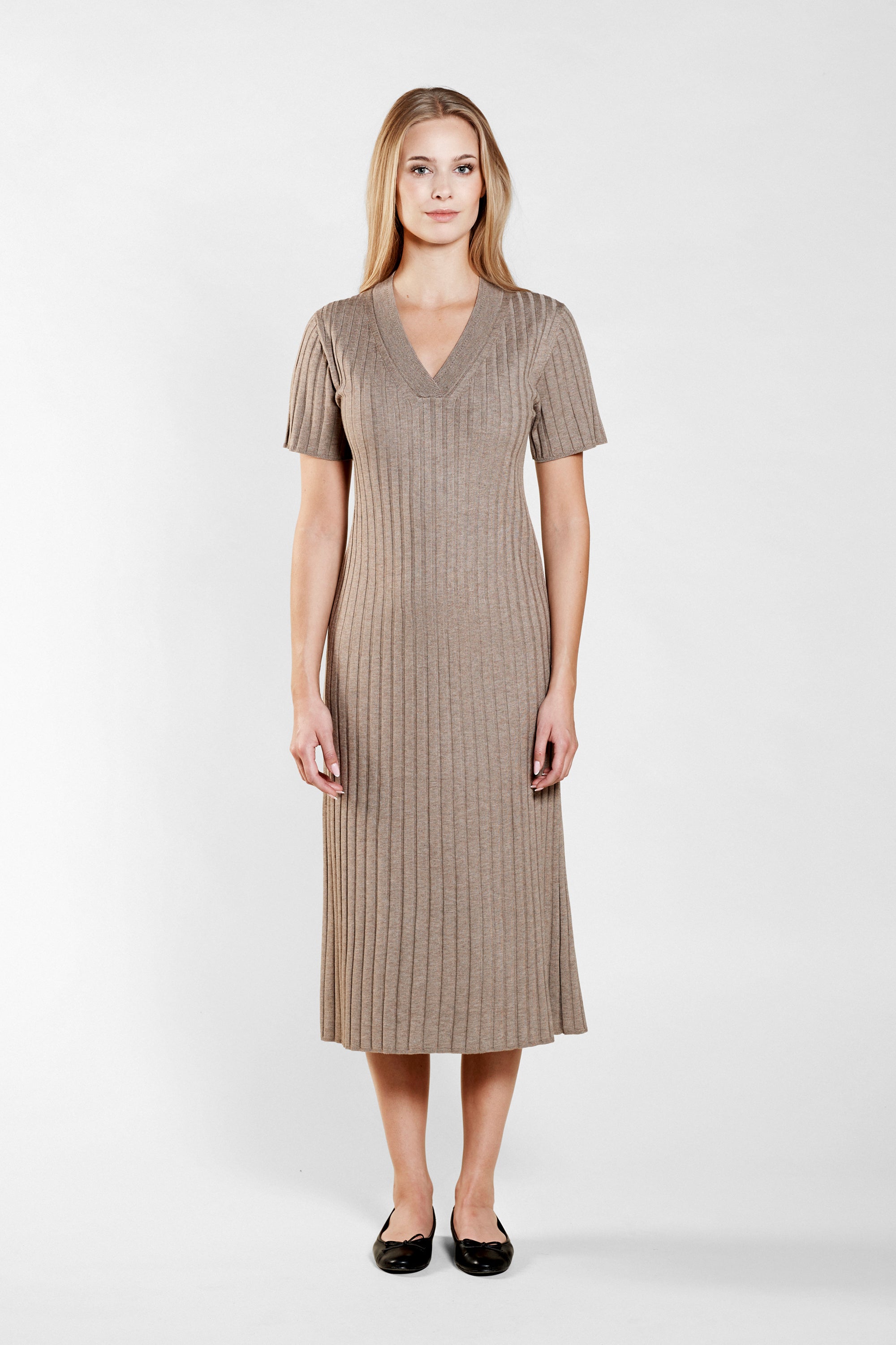 Smiling model presents a sophisticated V-neck knit dress by Cyme Copenhagen, crafted with natural materials, encapsulating the essence of sustainable, timeless Scandinavian fashion.