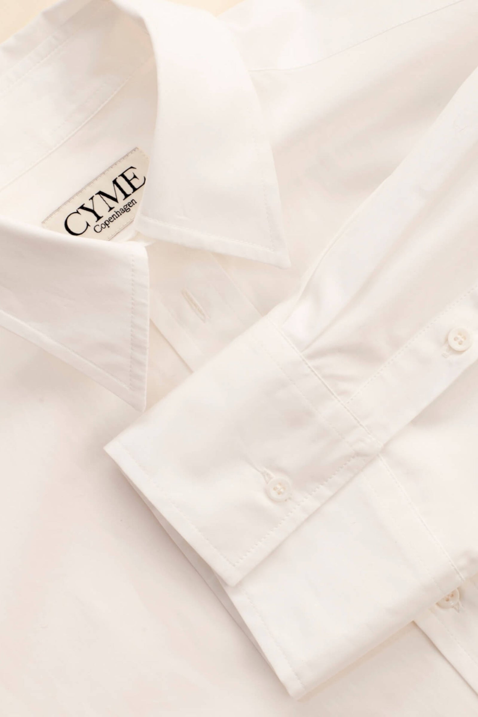 Detail of Cyme Copenhagen's minimalist white shirt with logo on the collar, embodying the clean and sustainable design of Scandinavian fashion.
