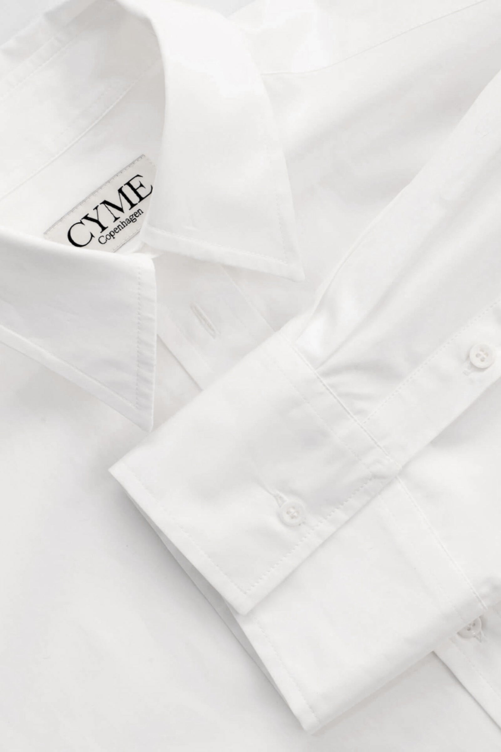 Detail of Cyme Copenhagen's minimalist white shirt with logo on the collar, embodying the clean and sustainable design of Scandinavian fashion.