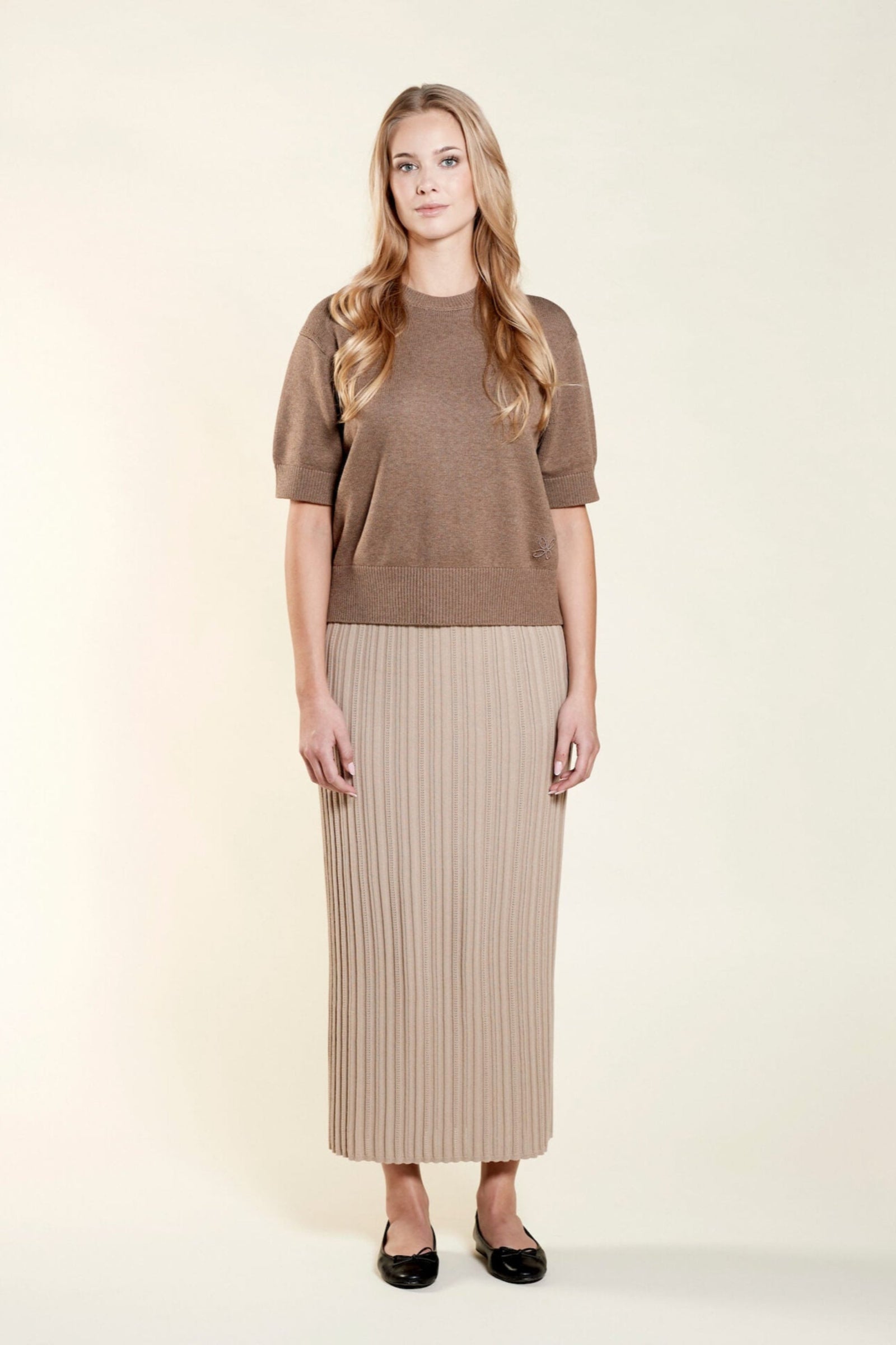 Confident model in a matching Cyme Copenhagen pointelle knit top and skirt set in soft beige, highlighting the brand's use of natural fibers for a sustainable and chic Scandinavian look.