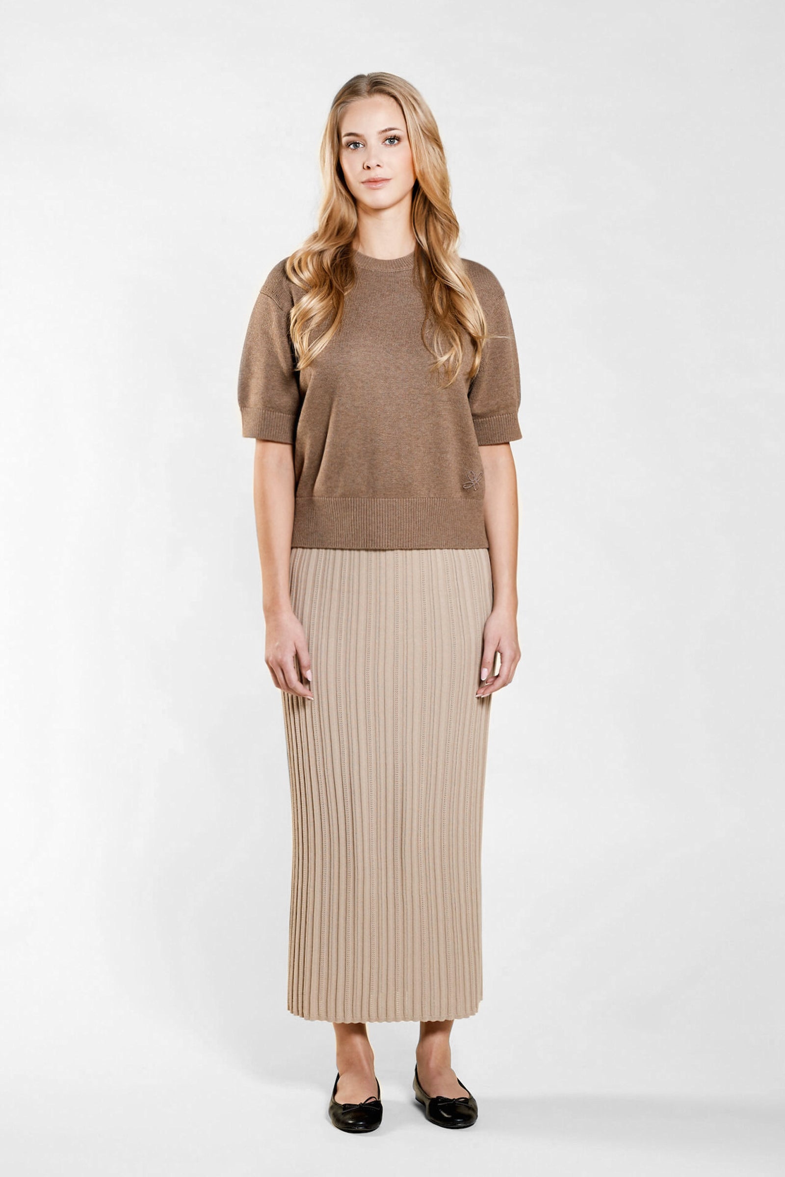 Confident model in a matching Cyme Copenhagen pointelle knit top and skirt set in soft beige, highlighting the brand's use of natural fibers for a sustainable and chic Scandinavian look.