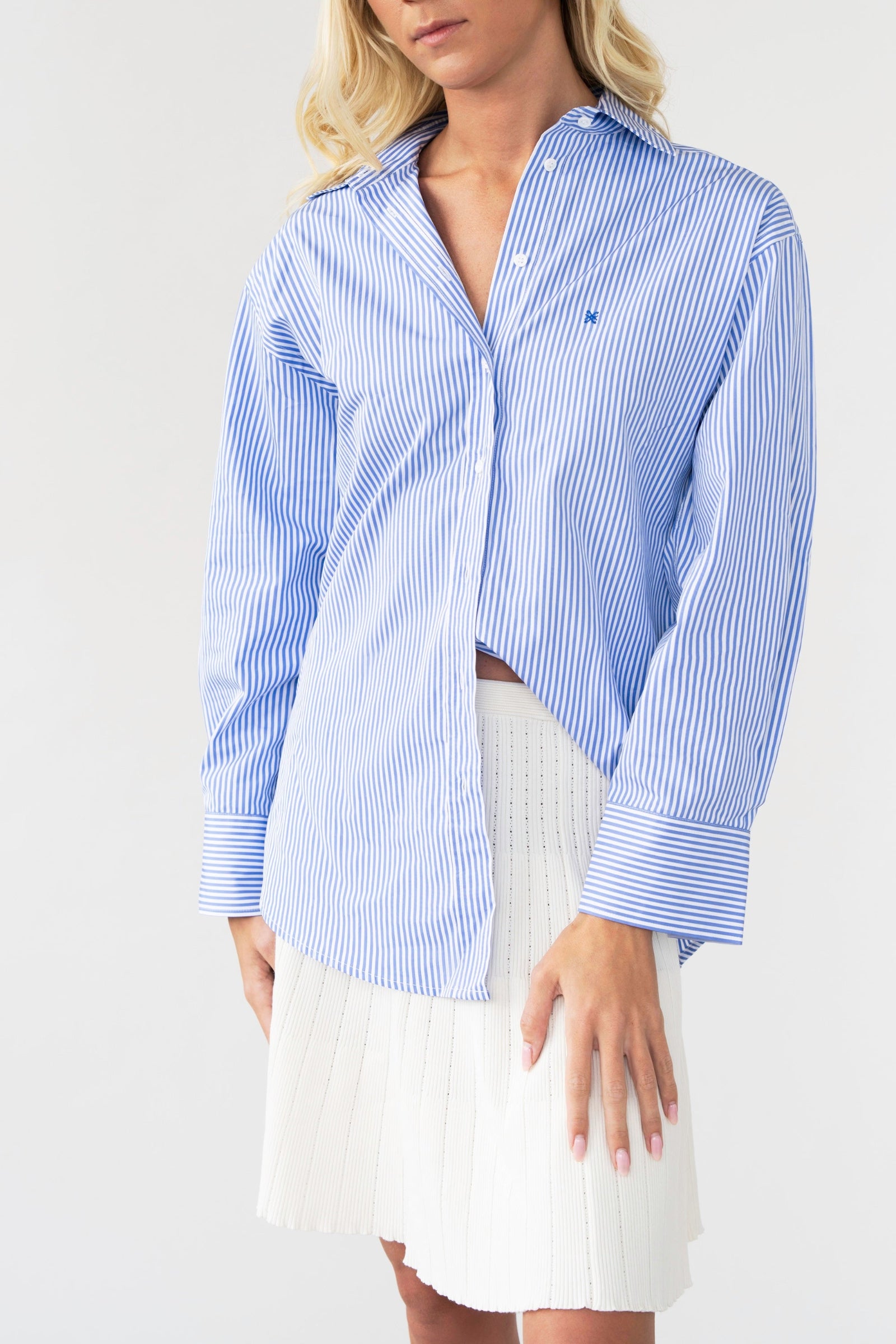 Woman wearing a blue and white striped shirt over a white skirt on a plain background