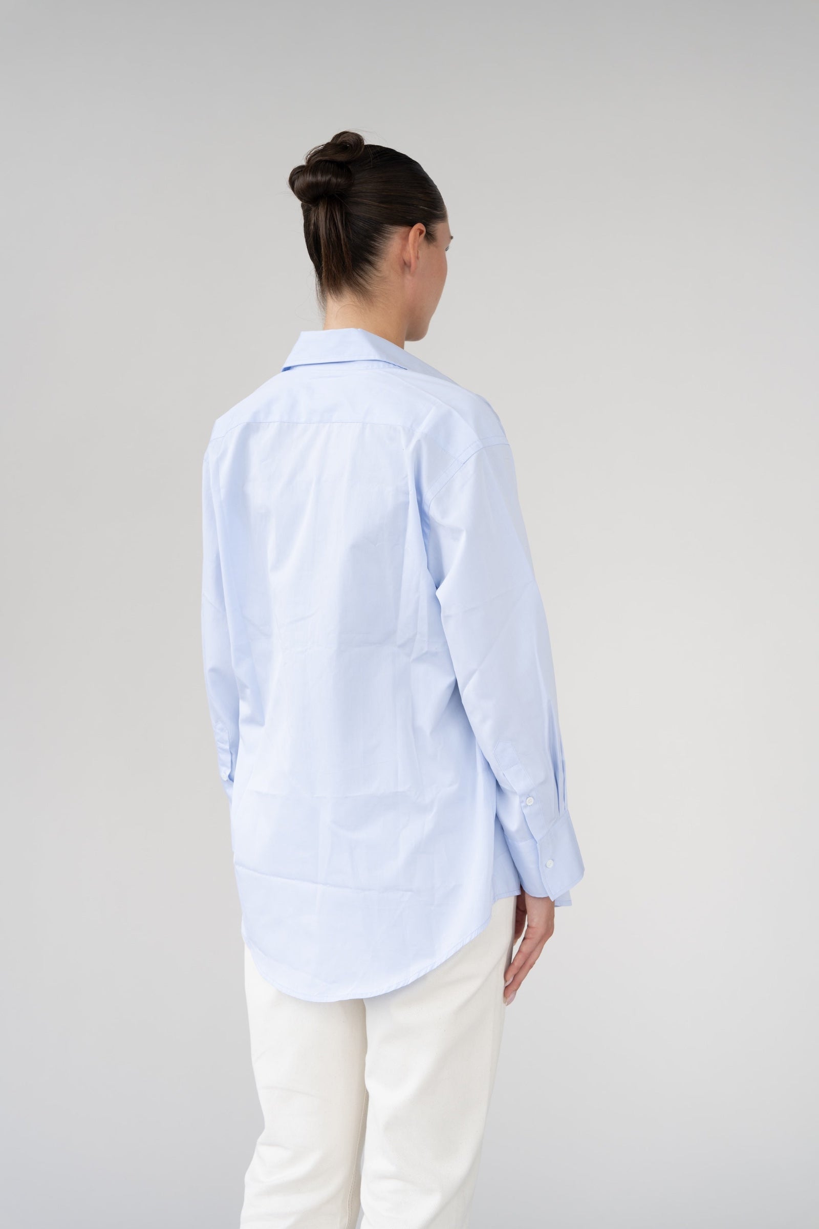 Person wearing a light blue shirt and white pants on a plain background