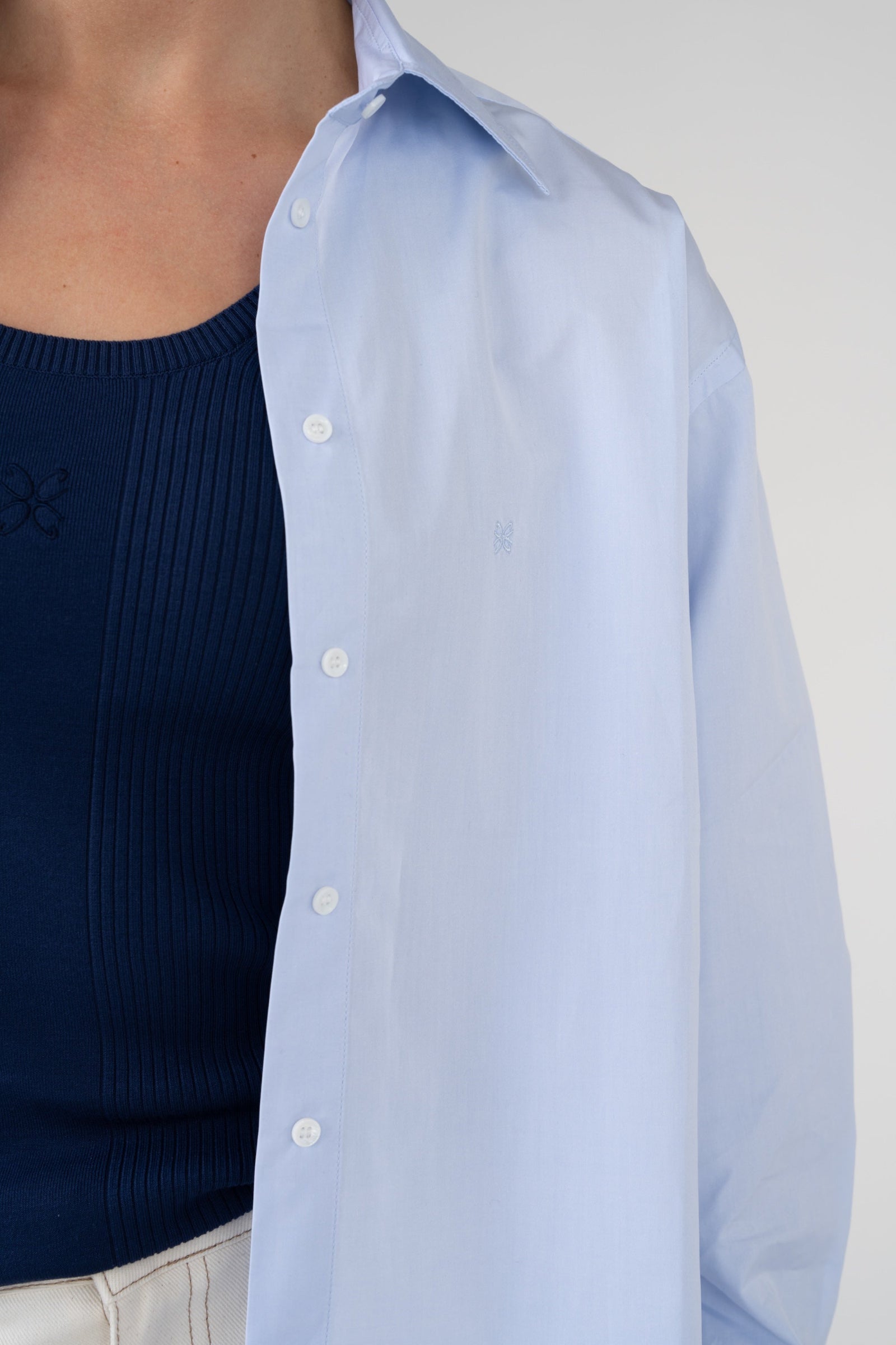 Light blue button-up shirt over a navy sweater on a plain background