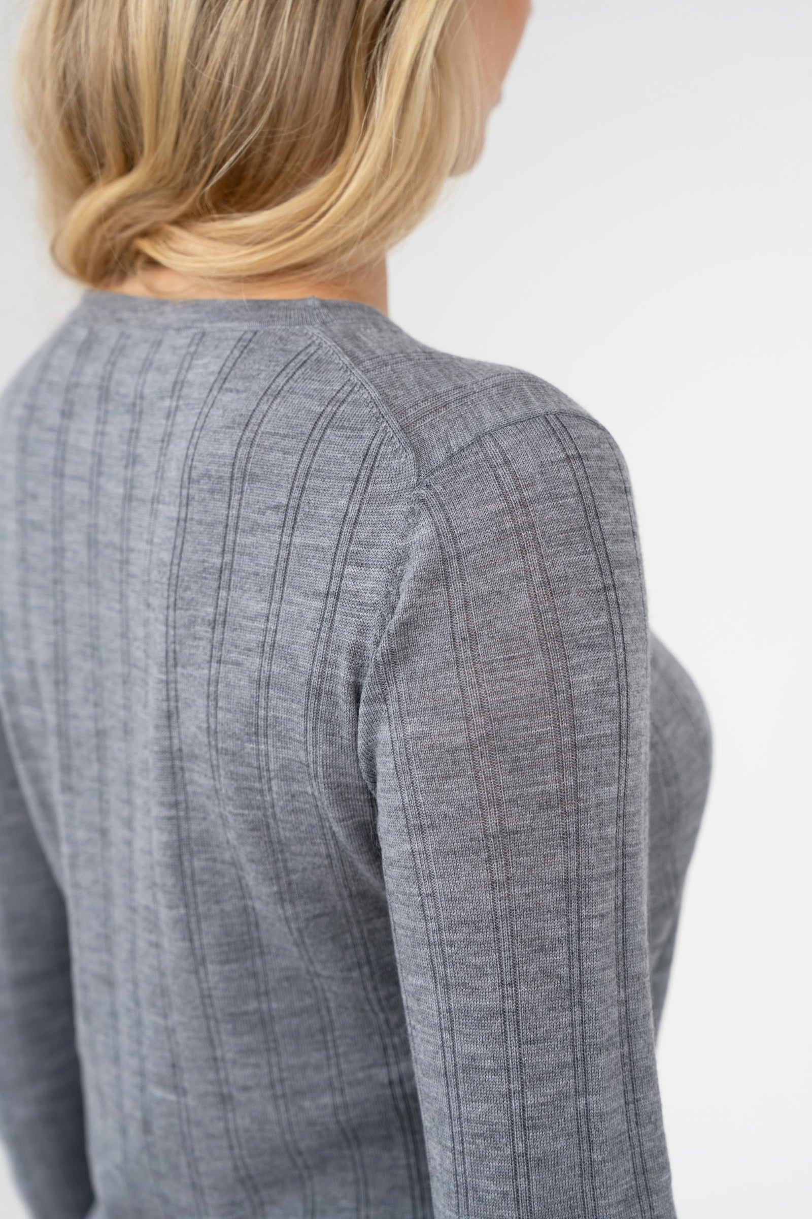 Close-up on-model shoulder seam detail of ribbed crew-neck sweater, grey, studio.