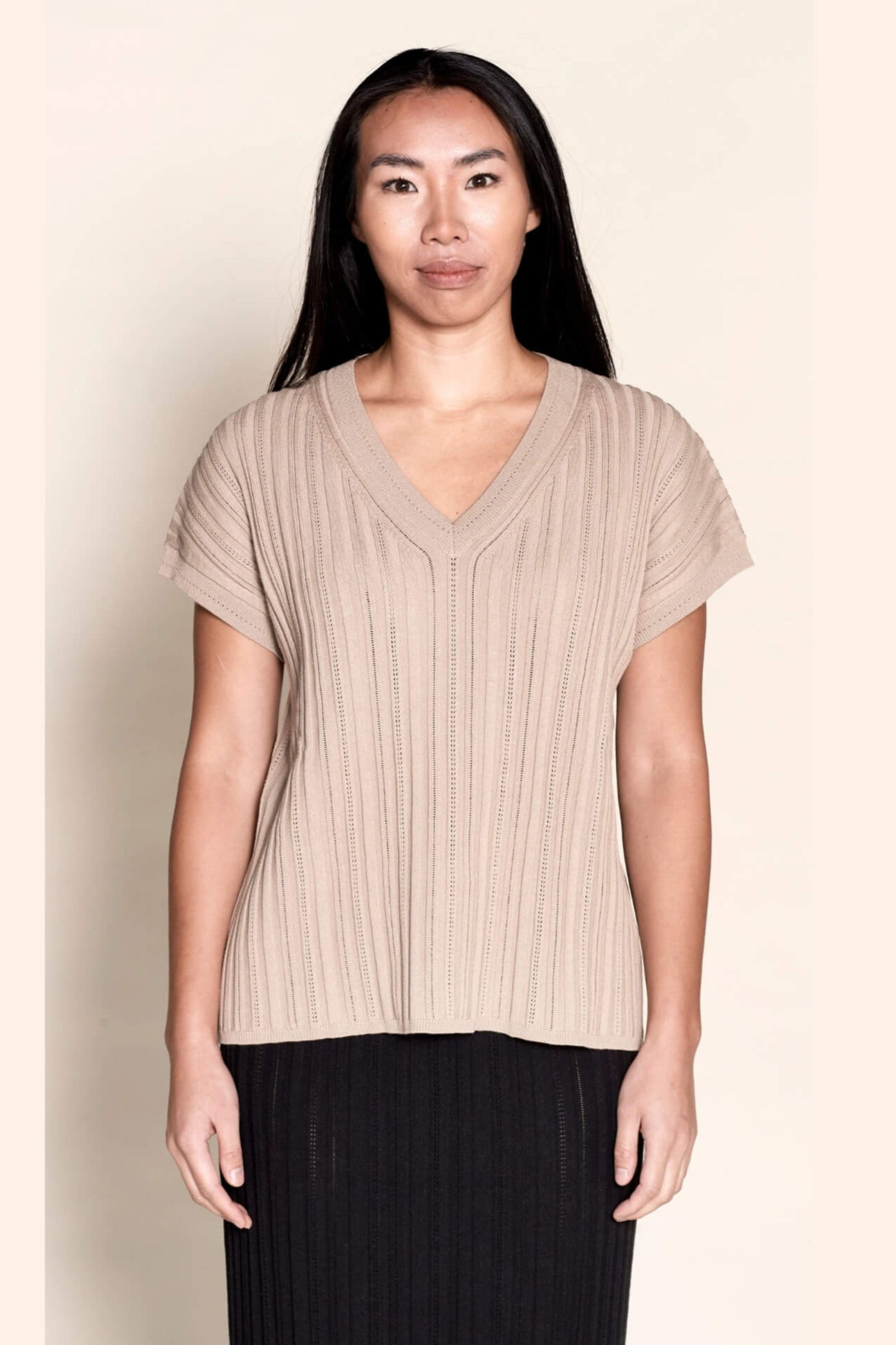 Model presents a taupe V-neck knit top by Cyme Copenhagen, exemplifying the blend of sustainable fashion with Danish designer expertise, available in a clothing store that caters to fashion-forward.