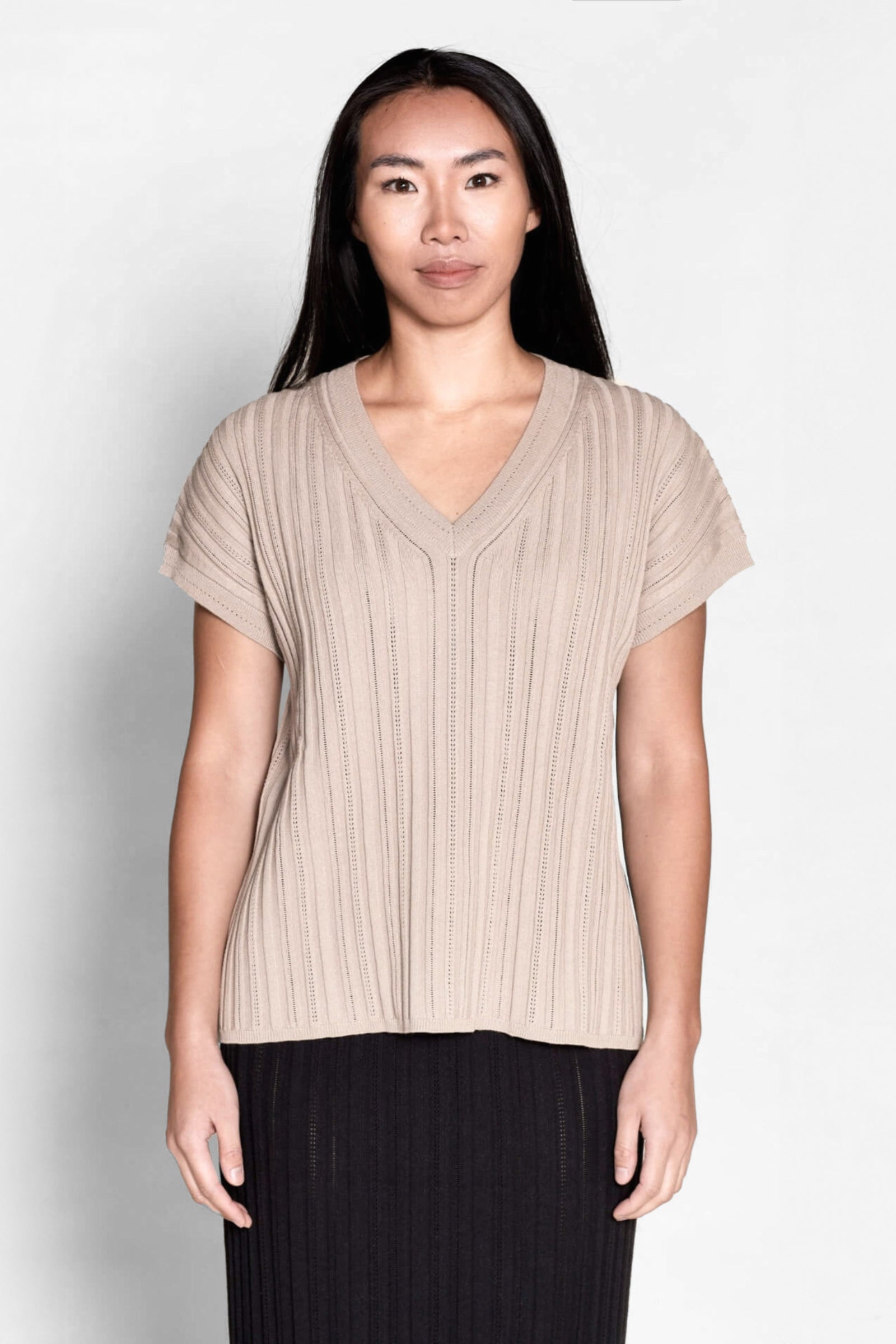 Model presents a taupe V-neck knit top by Cyme Copenhagen, exemplifying the blend of sustainable fashion with Danish designer expertise, available in a clothing store that caters to fashion-forward.
