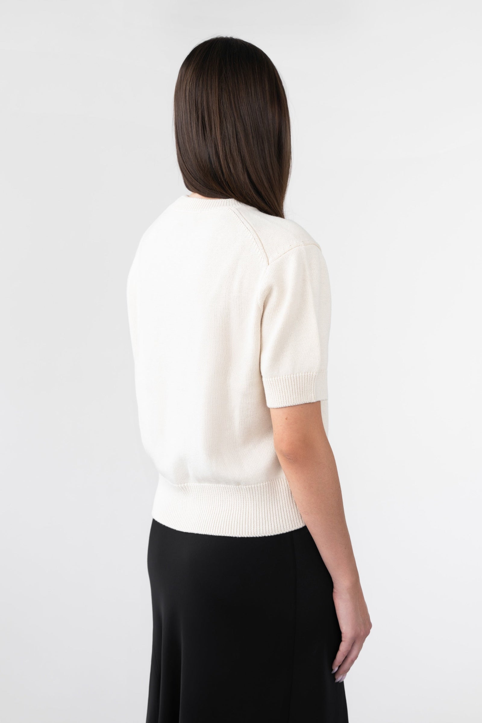 A woman wearing a white knitted tee and a black satin skirt against a gray background.