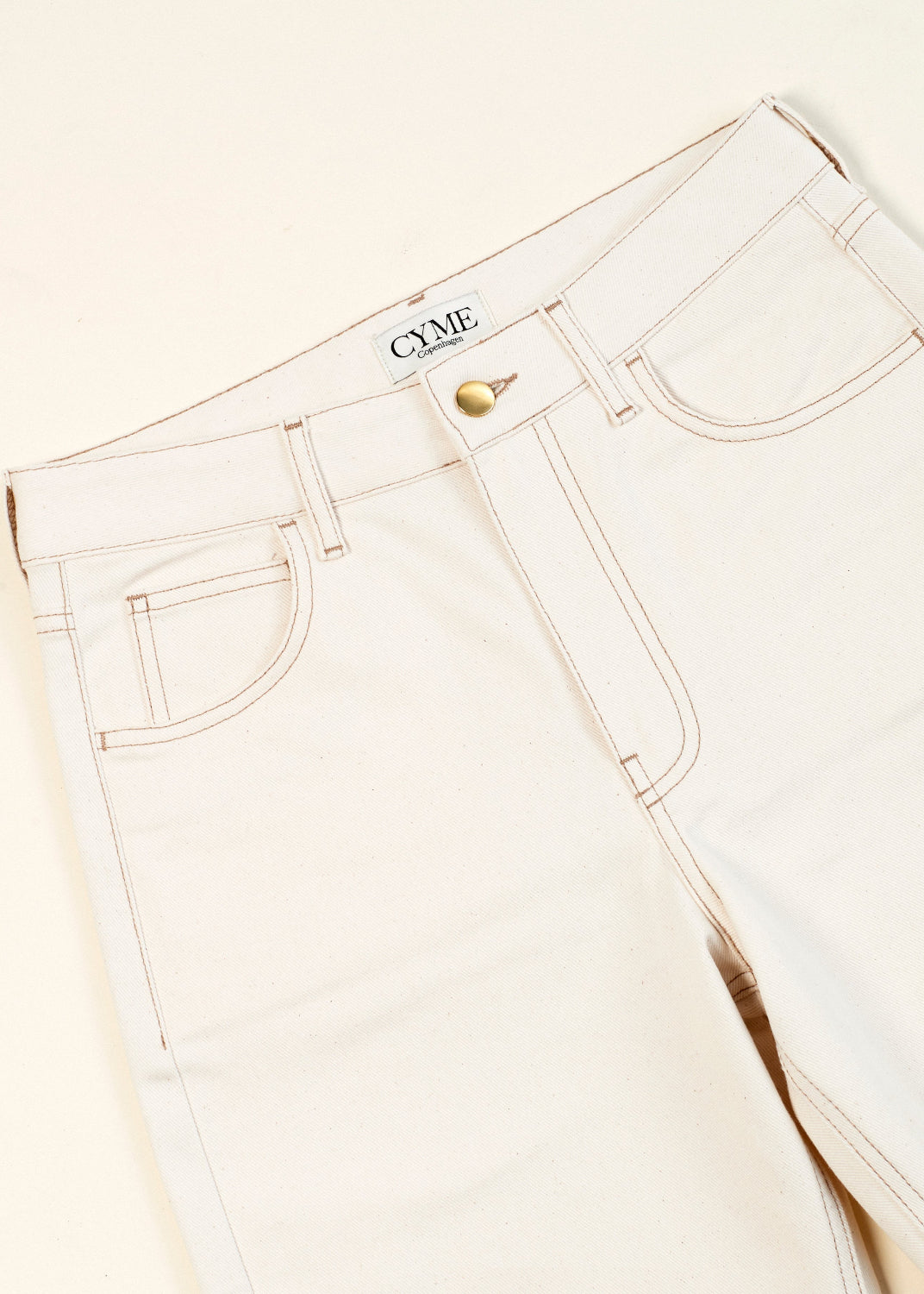 White jeans with a brand logo on a light beige background