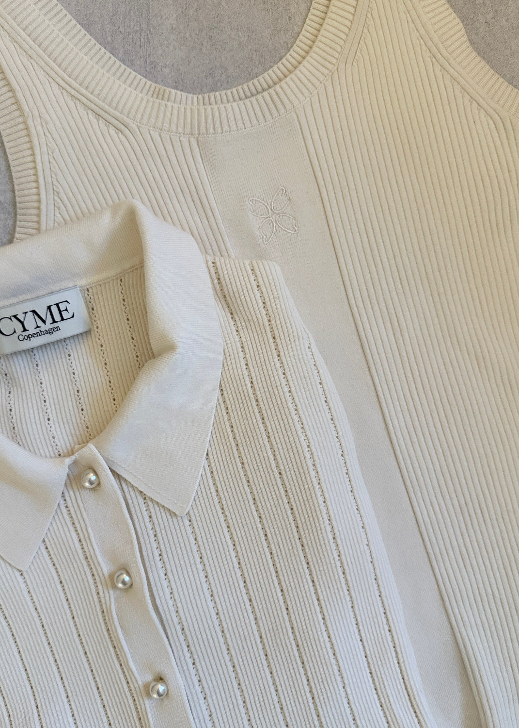White ribbed sweater with a collar and button details, featuring the Cyme brand label.