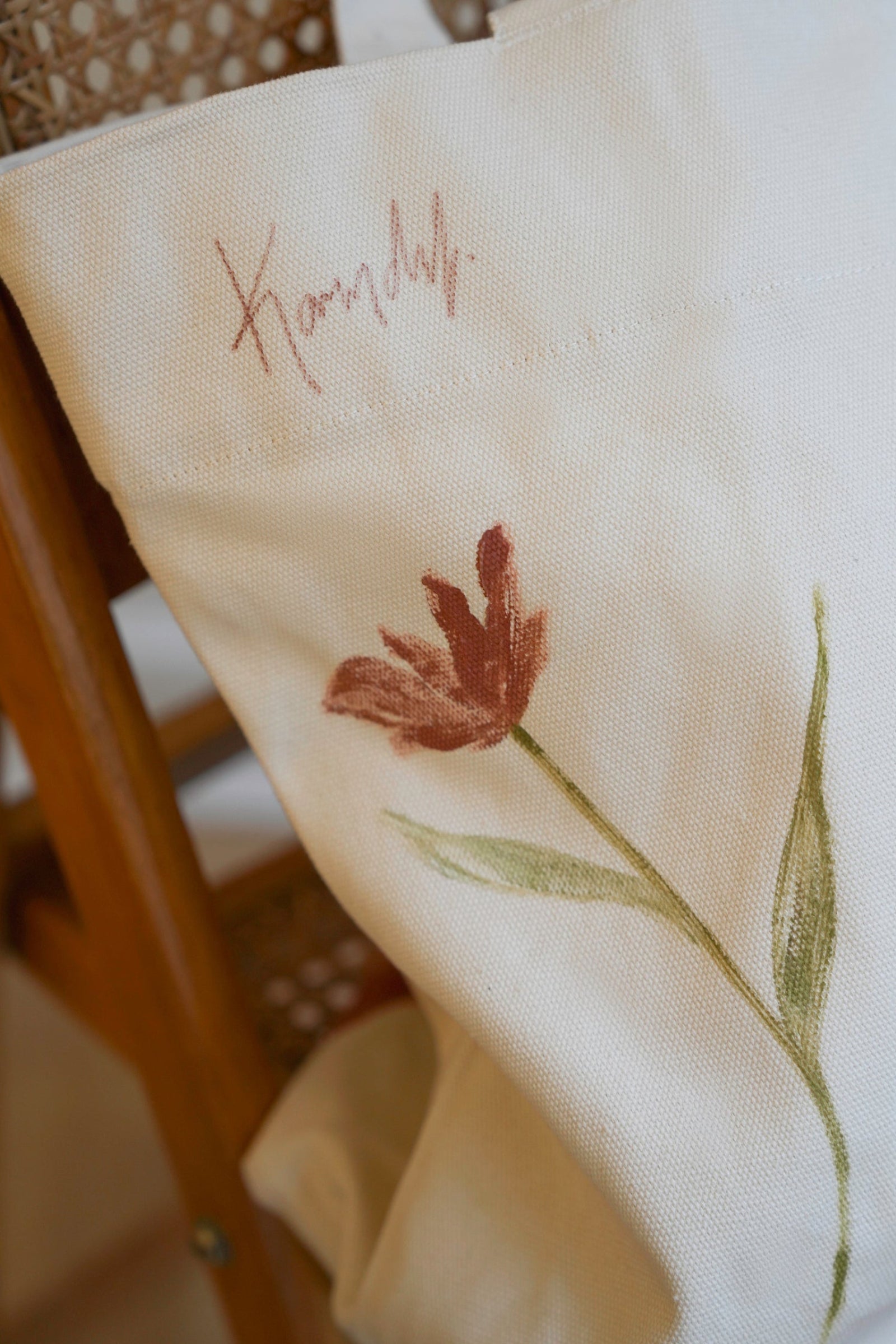 Decorative pillow with floral embroidery and Karen Dulong signature on a wooden chair.