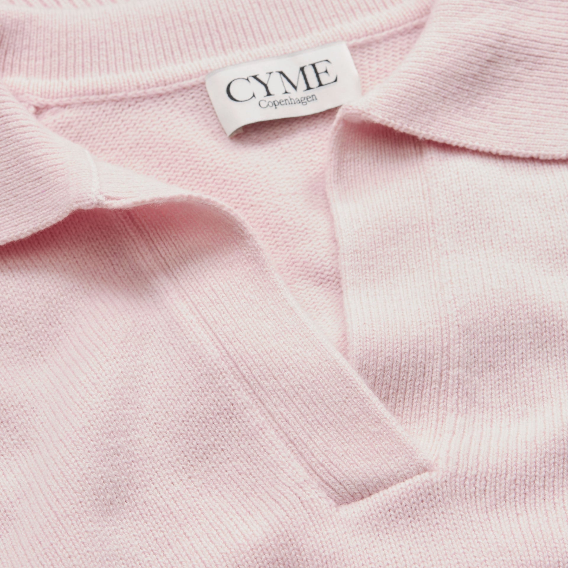 A close-up of the collar and neckline of a light pink polo-style knit jumper, featuring a "CYME Copenhagen" label.