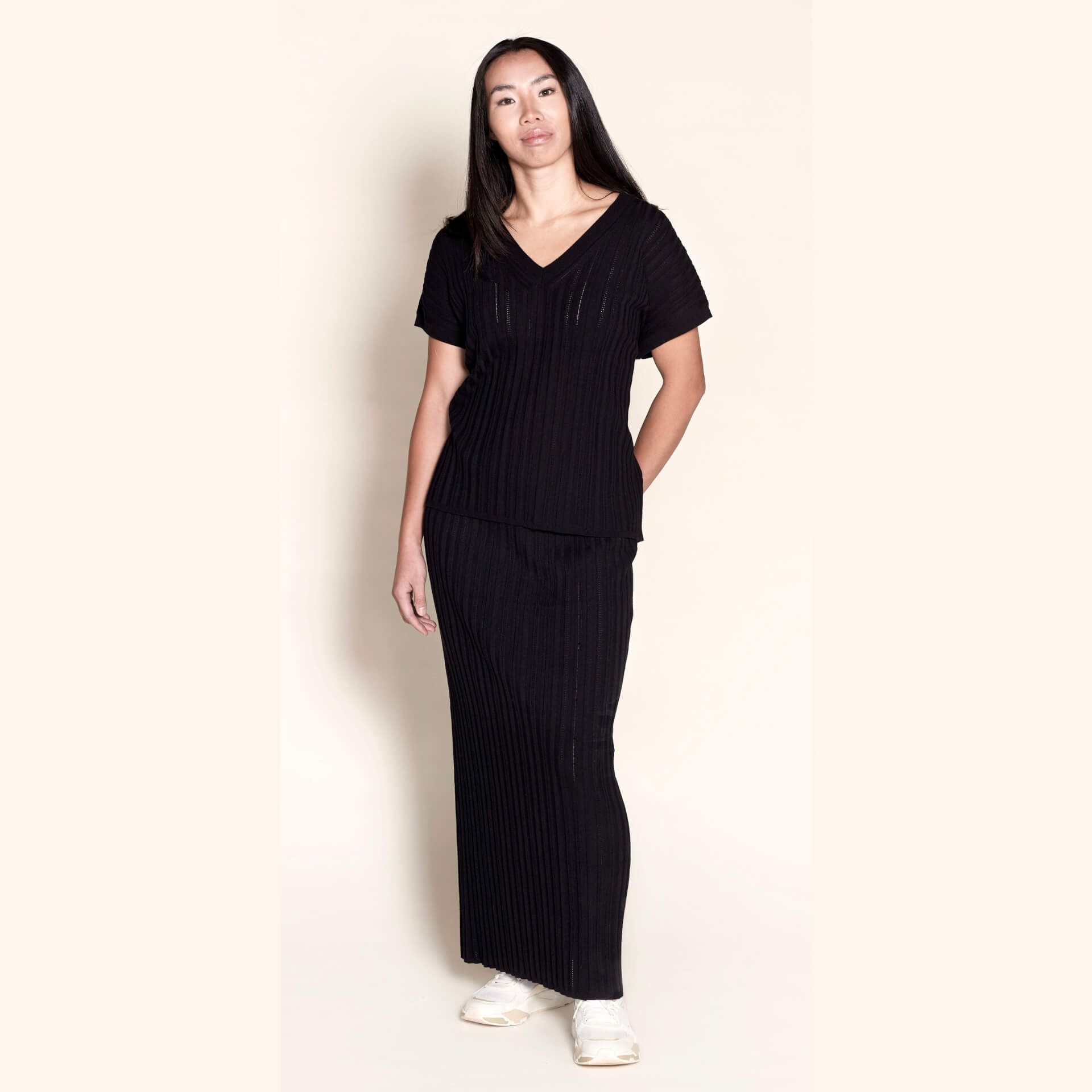 Model elegantly dons a Cyme Copenhagen all-black ribbed knit ensemble, featuring a V-neck top and matching skirt, a chic example of the brand's sustainable fashion offerings in women's clothing from a top Danish designer.