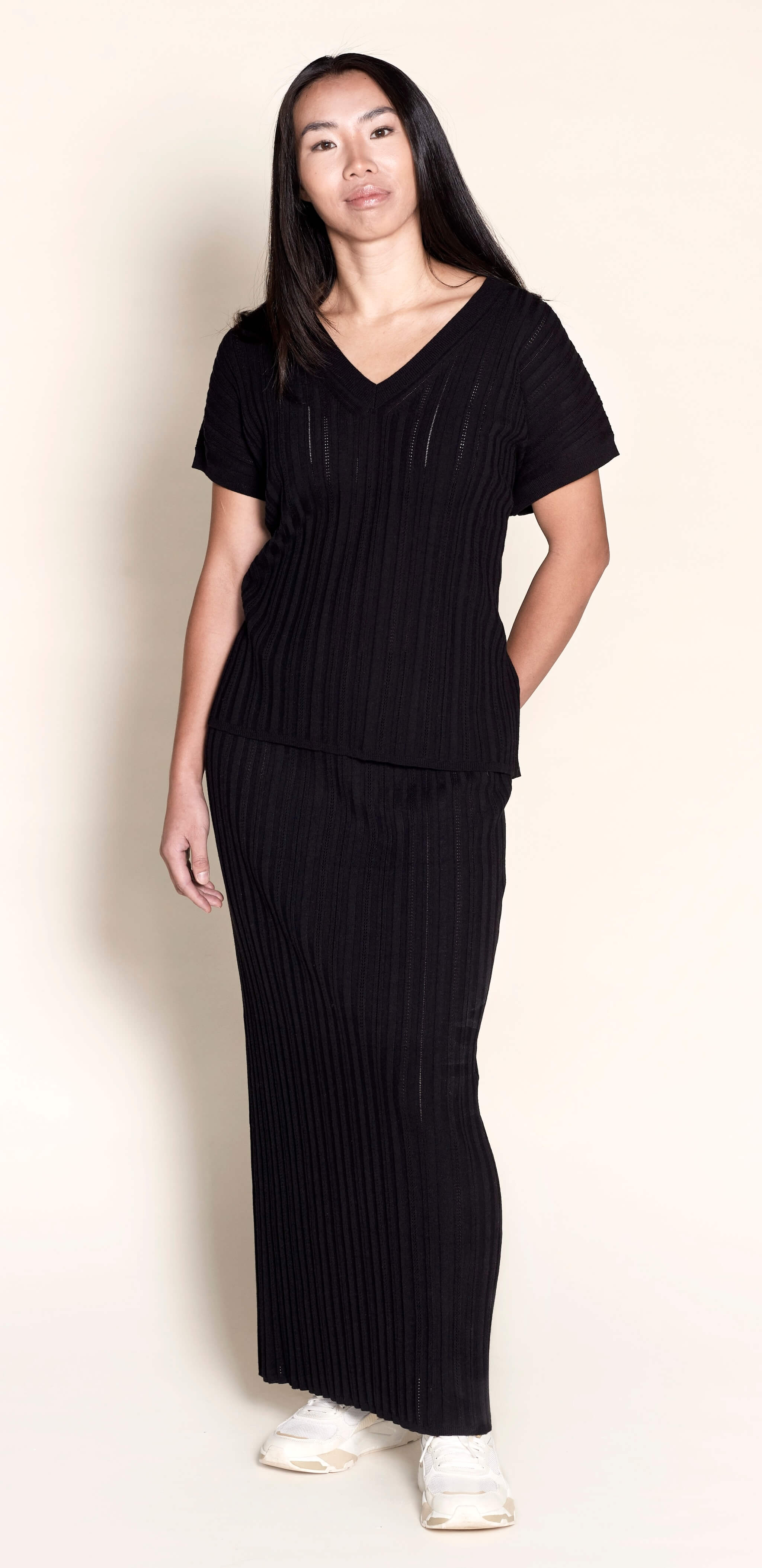 Model elegantly dons a Cyme Copenhagen all-black ribbed knit ensemble, featuring a V-neck top and matching skirt, a chic example of the brand's sustainable fashion offerings in women's clothing from a top Danish designer.