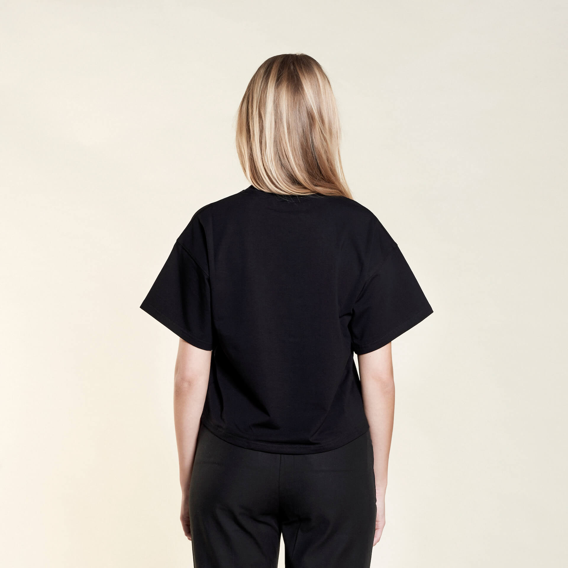 Rear view of a woman wearing a black t-shirt from Cyme Copenhagen's spring/summer collection. The t-shirt has a simple and relaxed fit, showcasing the clean lines and minimalist design. The model stands against a neutral background, highlighting the versatility and casual elegance of the garment.