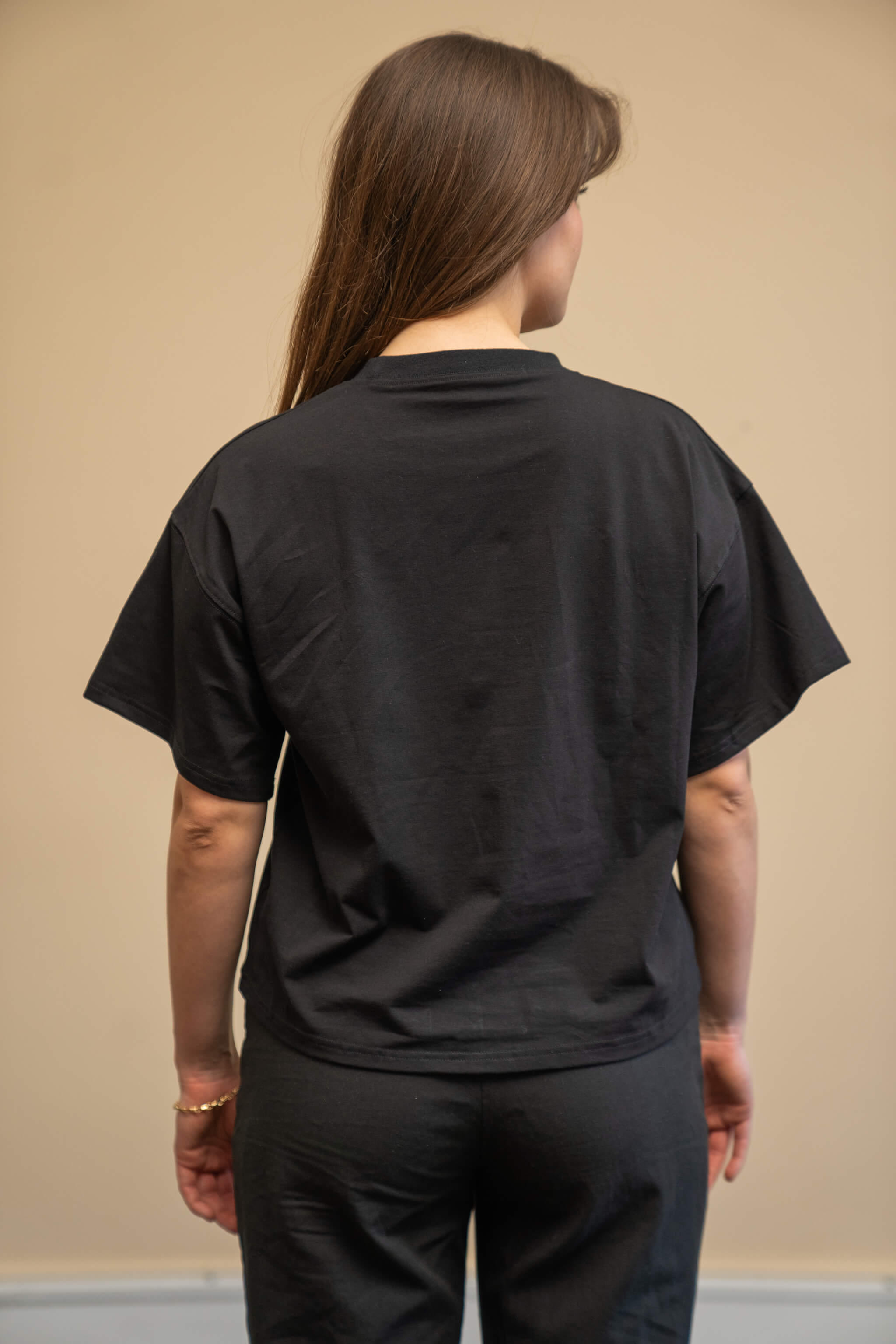 Rear view of a woman wearing a black t-shirt from Cyme Copenhagen's spring/summer collection. The t-shirt has a simple and relaxed fit, showcasing the clean lines and minimalist design. The model stands against a neutral background, highlighting the versatility and casual elegance of the garment.