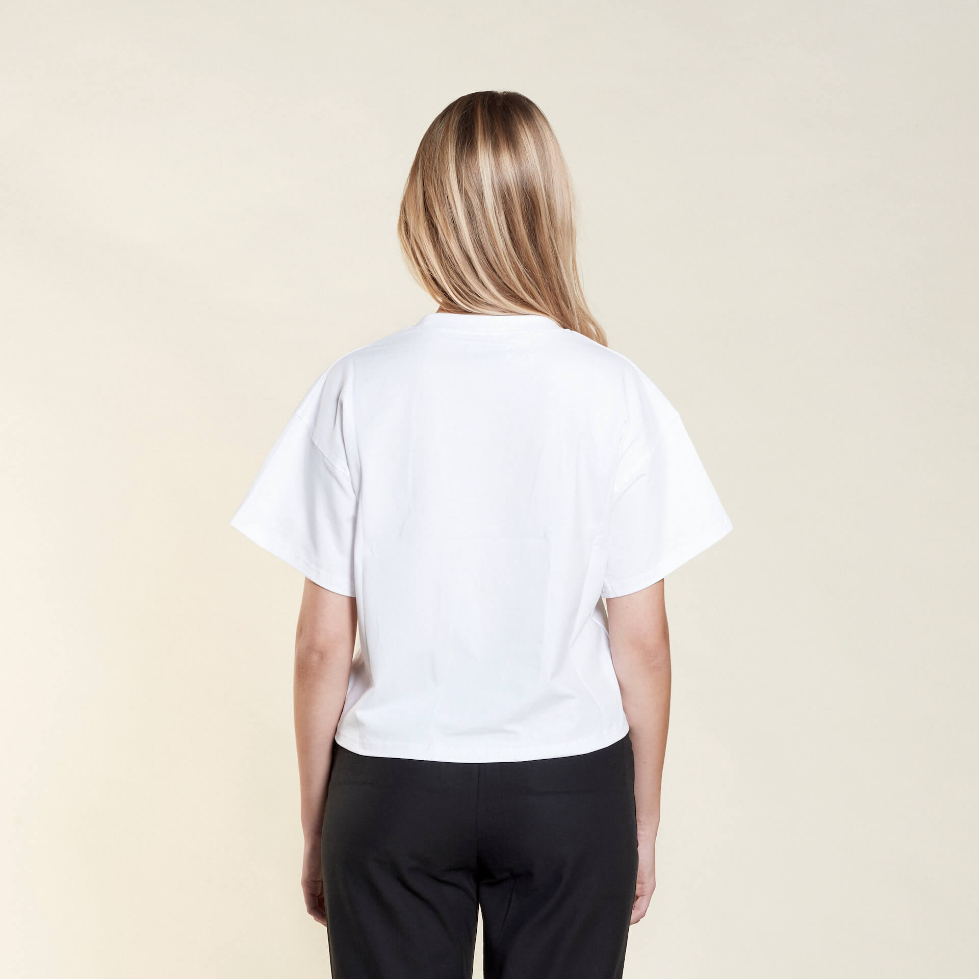 Rear view of a woman wearing a white t-shirt from Cyme Copenhagen's spring/summer collection. The t-shirt has a simple and relaxed fit, showcasing the clean lines and minimalist design. The model stands against a neutral background, emphasizing the versatility and casual elegance of the garment.