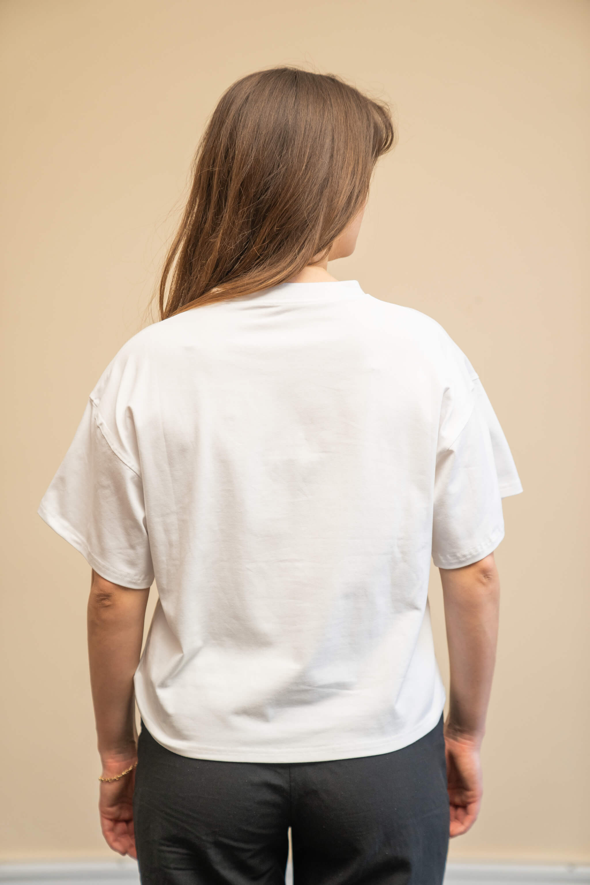 Rear view of a woman wearing a white t-shirt from Cyme Copenhagen's spring/summer collection. The t-shirt has a simple and relaxed fit, showcasing the clean lines and minimalist design. The model stands against a neutral background, emphasizing the versatility and casual elegance of the garment.
