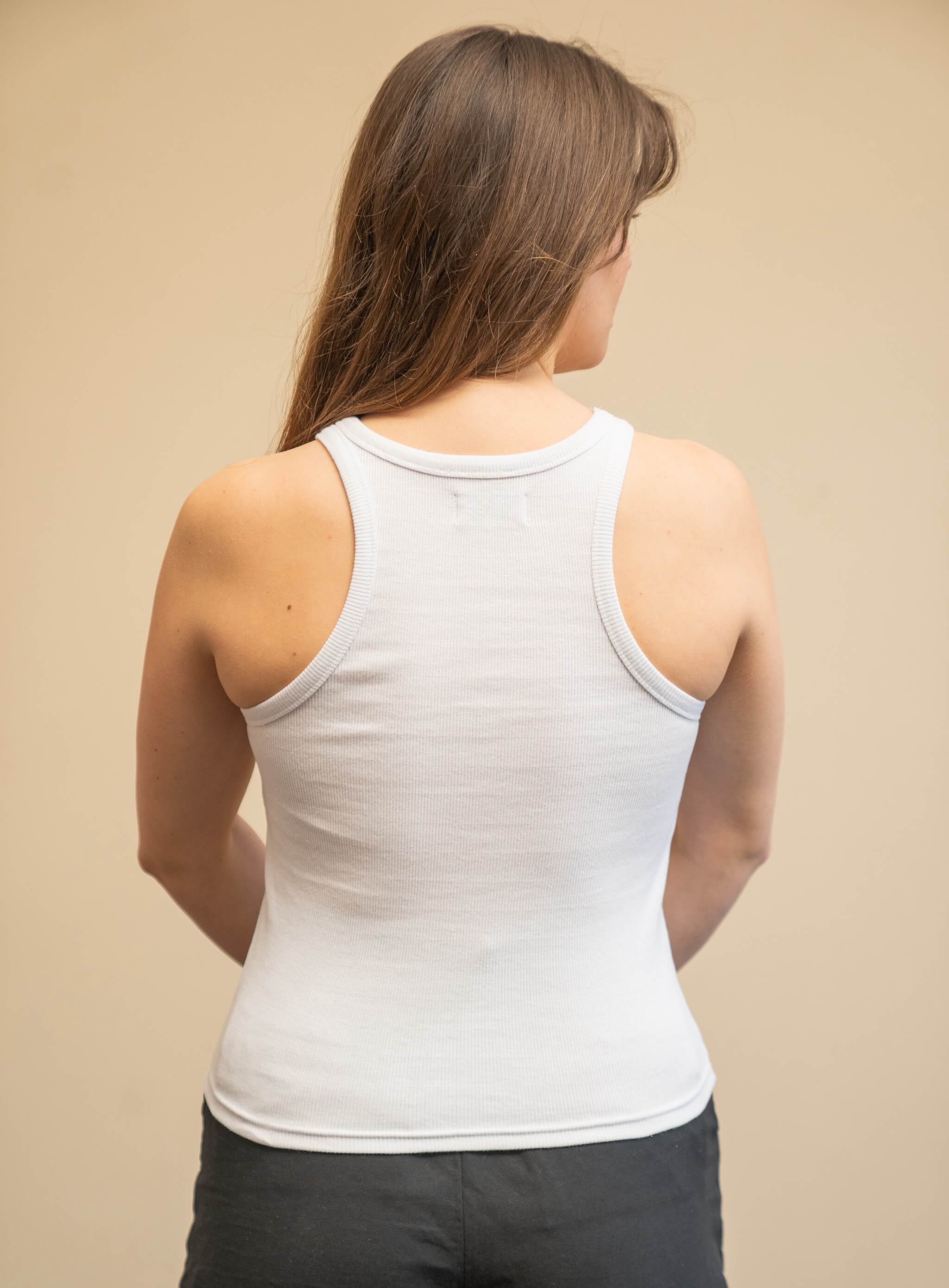 Rear view of a woman wearing a white tank top from Cyme Copenhagen's spring/summer collection. The tank top features a simple and sleek design with racerback styling. The model stands against a neutral background, highlighting the clean lines and minimalist appeal of the garment.