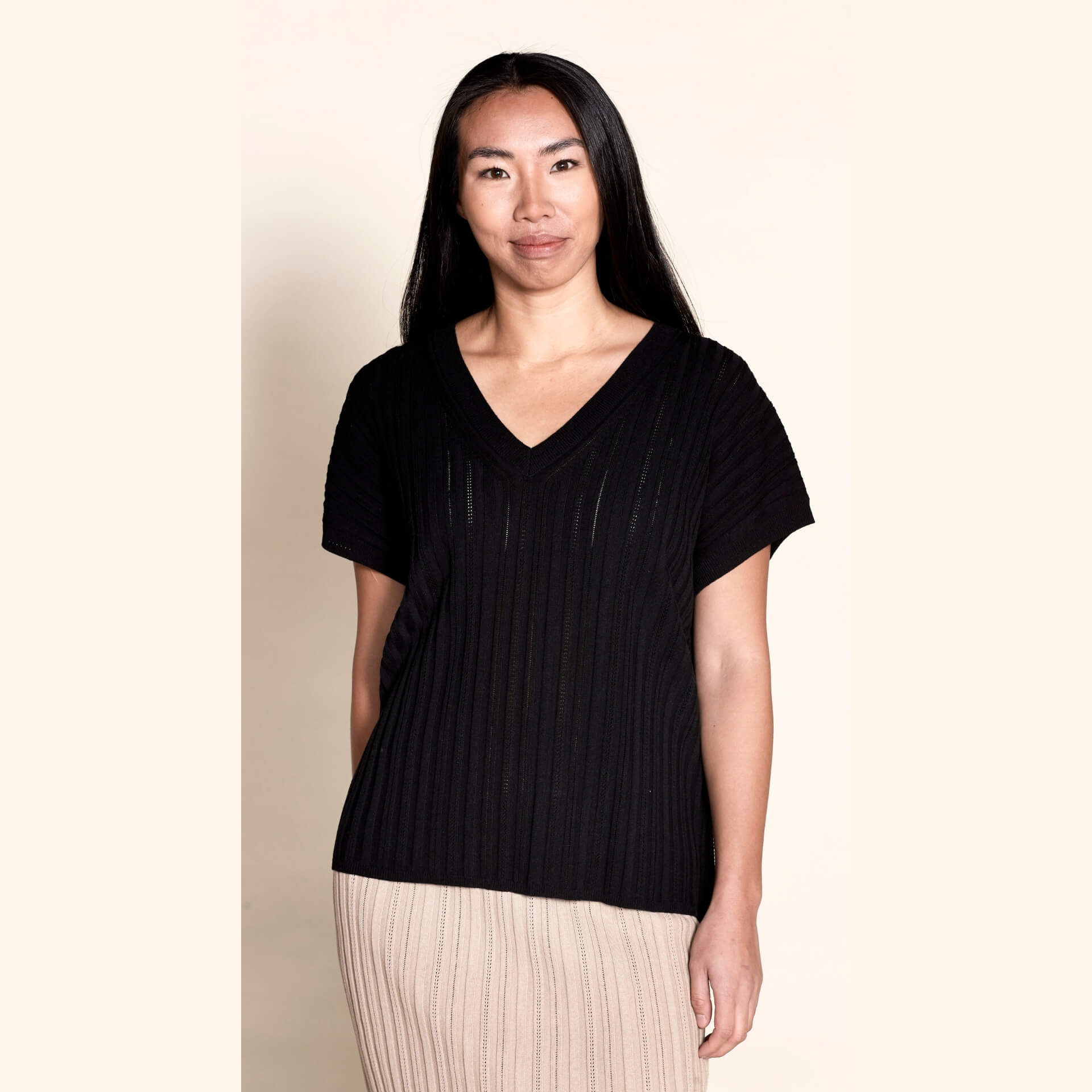 A model dons a Cyme Copenhagen black pointelle ribbed V-neck top, a perfect blend of modern style and sustainable craftsmanship from a leading Scandinavian fashion brand.