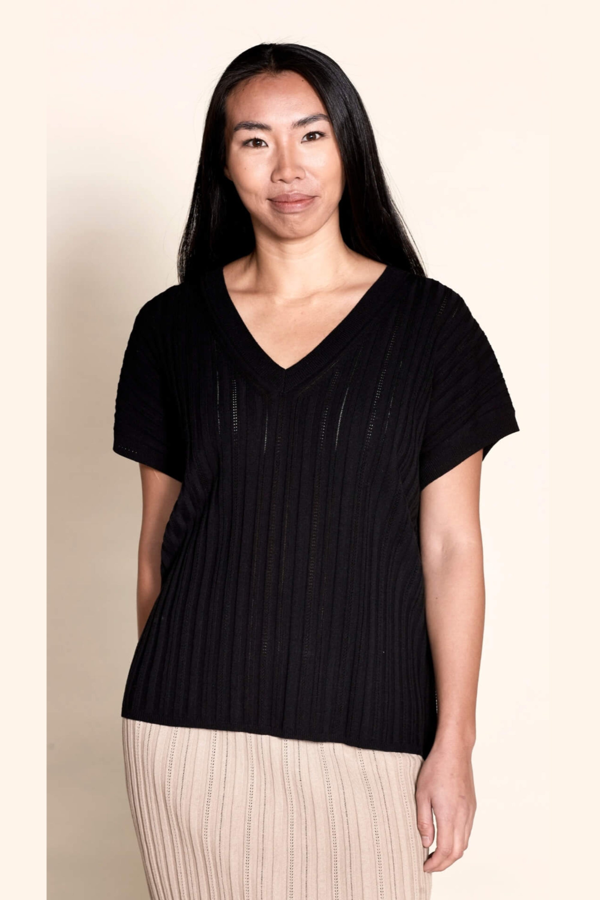 A model dons a Cyme Copenhagen black pointelle ribbed V-neck top, a perfect blend of modern style and sustainable craftsmanship from a leading Scandinavian fashion brand.