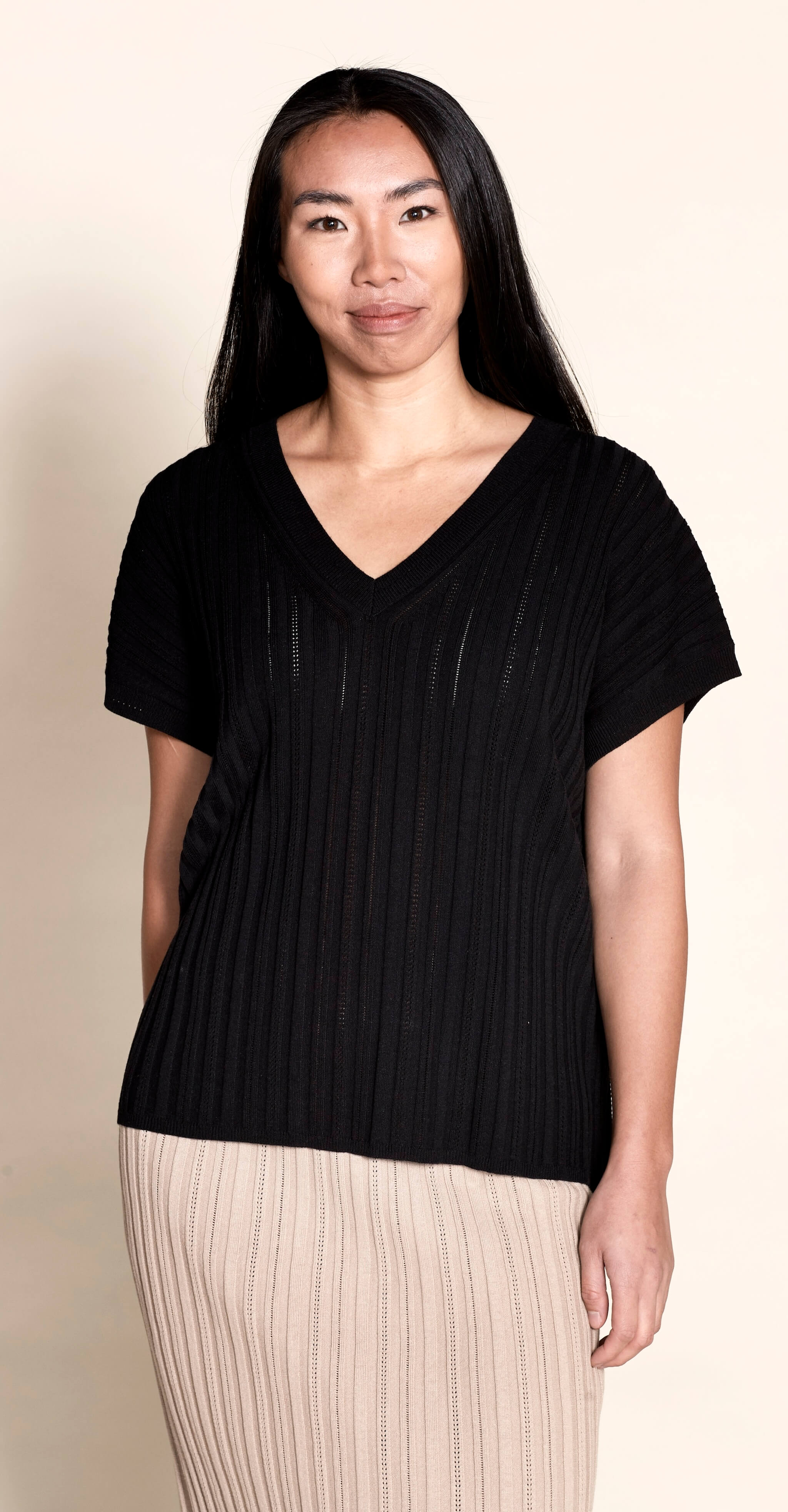 A model dons a Cyme Copenhagen black pointelle ribbed V-neck top, a perfect blend of modern style and sustainable craftsmanship from a leading Scandinavian fashion brand.