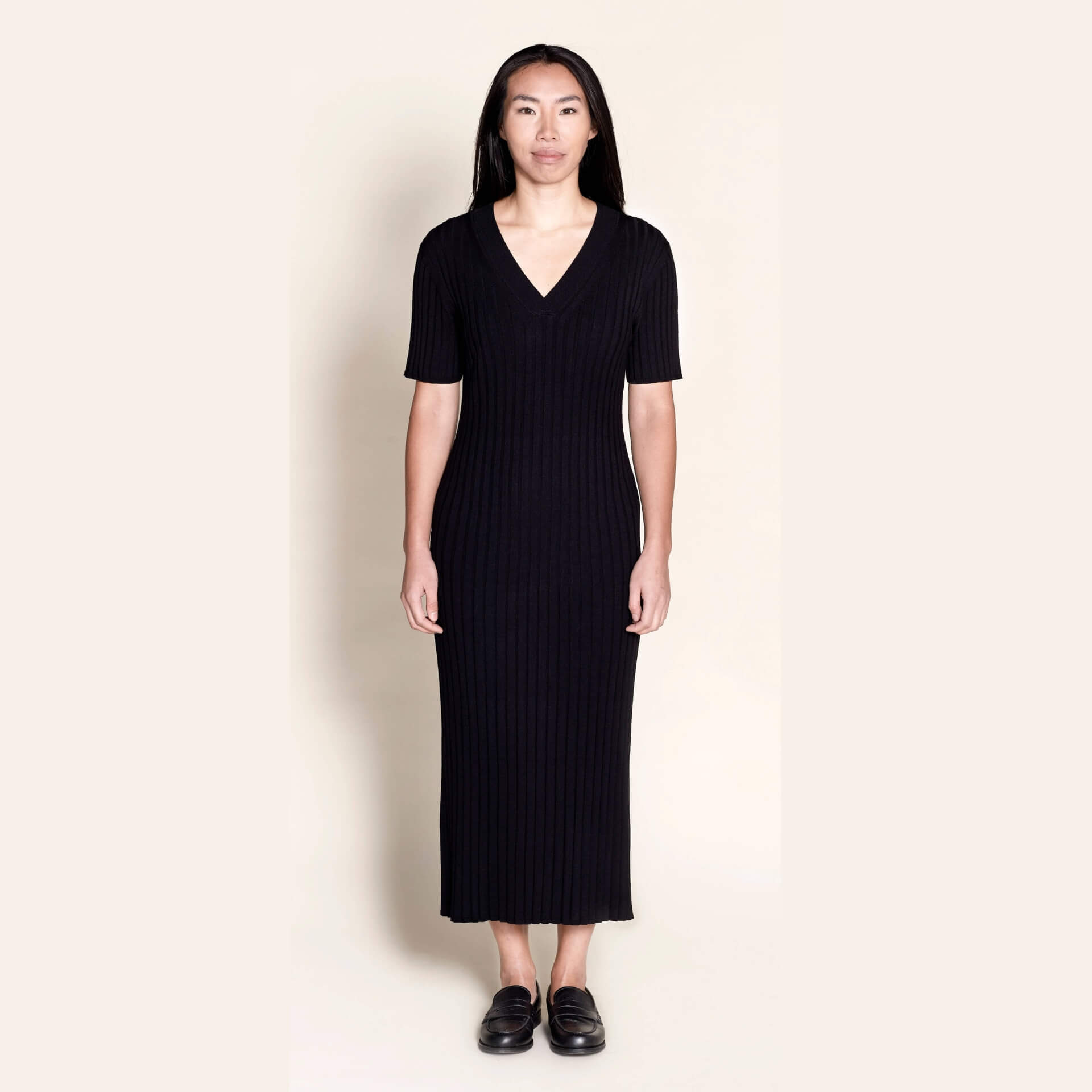 Model wears Cyme Copenhagen's classic black ribbed knit midi dress, featuring a flattering V-neck and short sleeves, a testament to sustainable, versatile women's fashion by a Danish designer.