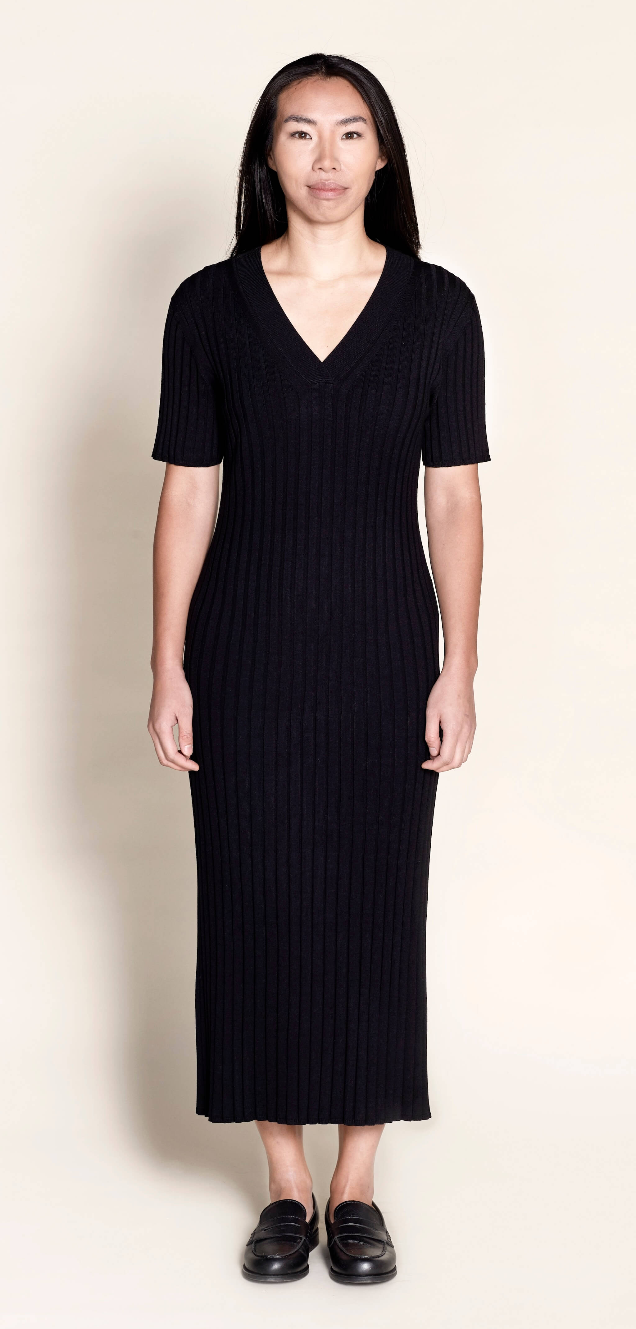 Model wears Cyme Copenhagen's classic black ribbed knit midi dress, featuring a flattering V-neck and short sleeves, a testament to sustainable, versatile women's fashion by a Danish designer.