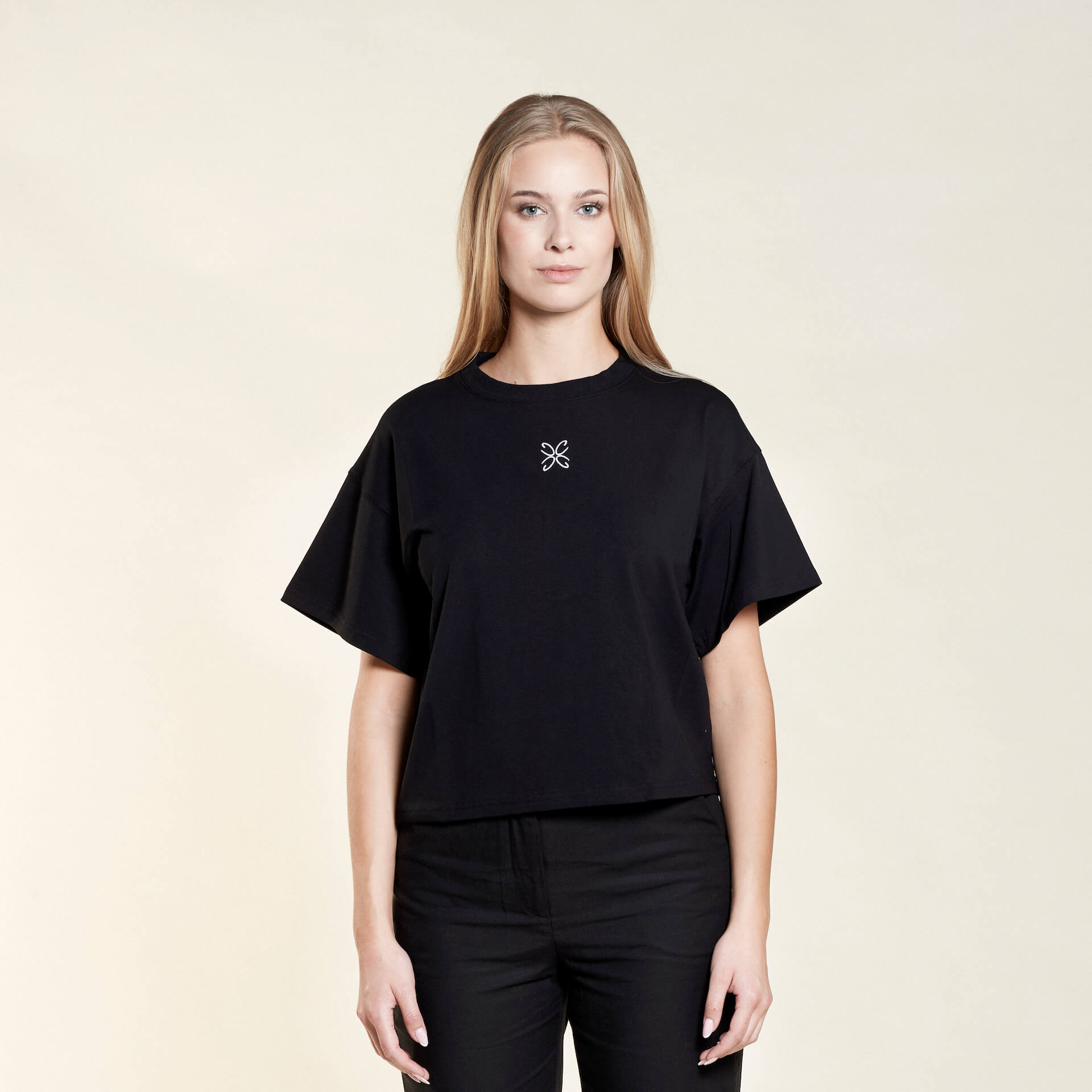 Woman wearing a black t-shirt from Cyme Copenhagen's spring/summer collection. The t-shirt features a simple, elegant design with a white logo in the center. The model stands against a neutral background, emphasizing the minimalist and stylish appeal of the garment.