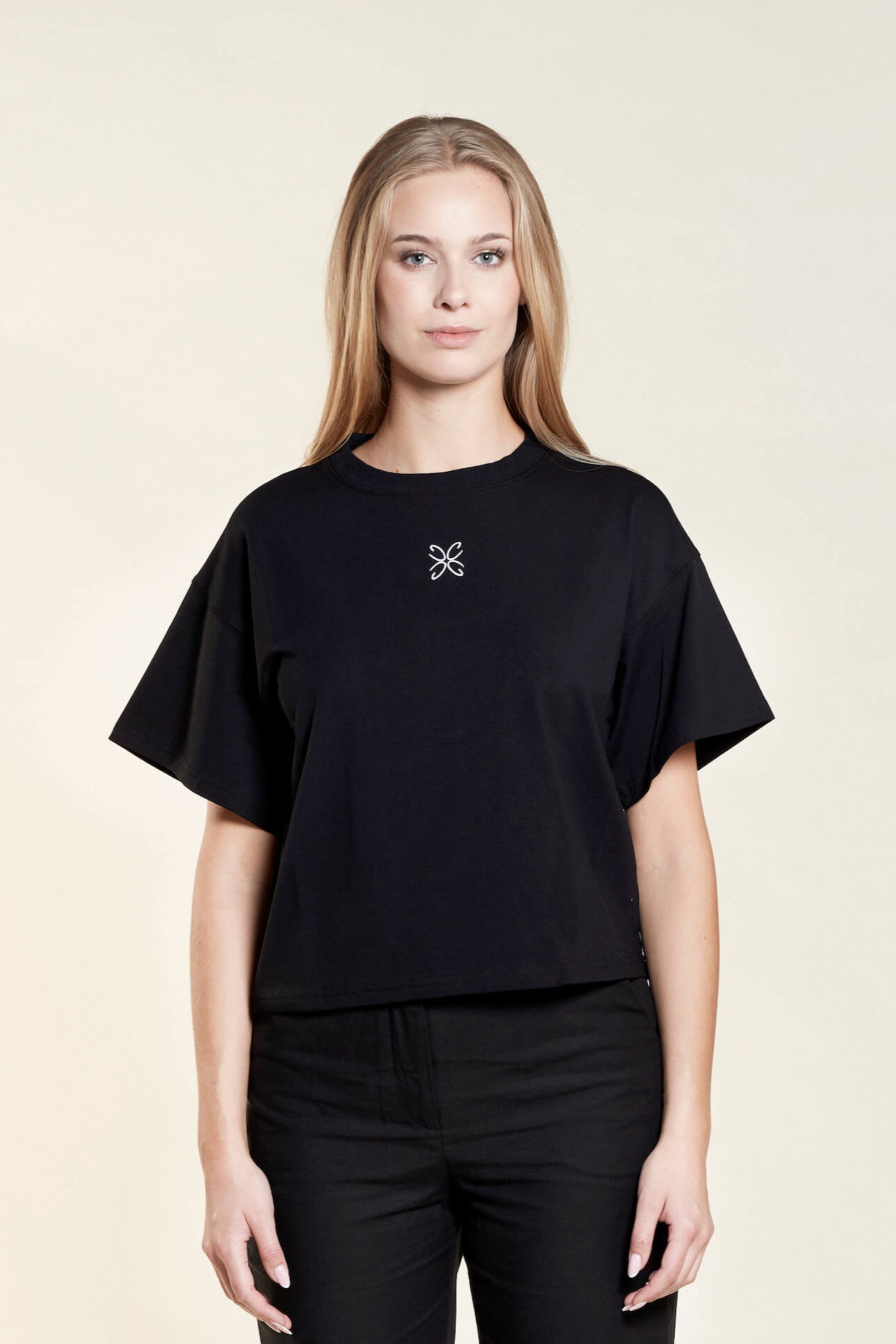 Woman wearing a black t-shirt from Cyme Copenhagen's spring/summer collection. The t-shirt features a simple, elegant design with a white logo in the center. The model stands against a neutral background, emphasizing the minimalist and stylish appeal of the garment.