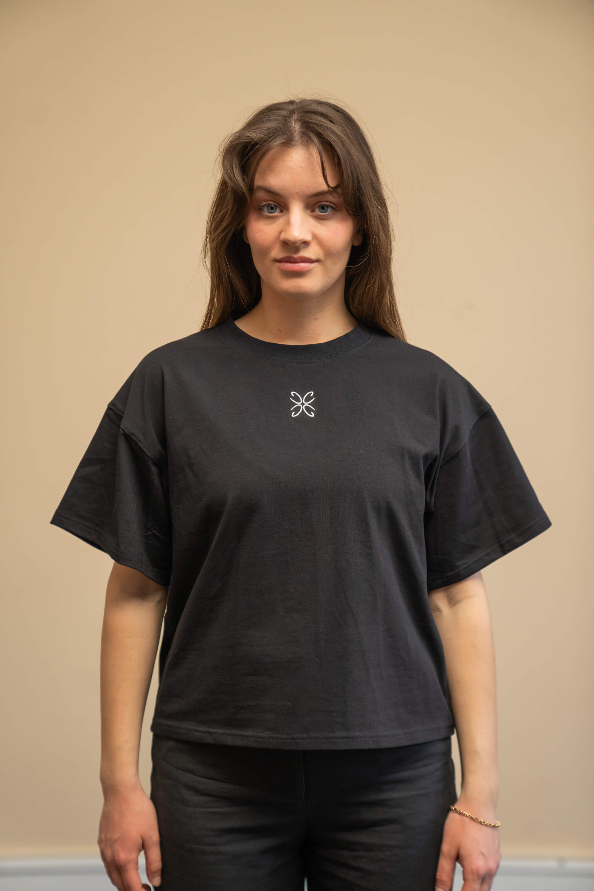 Woman wearing a black t-shirt from Cyme Copenhagen's spring/summer collection. The t-shirt features a simple, elegant design with a white logo in the center. The model stands against a neutral background, emphasizing the minimalist and stylish appeal of the garment.