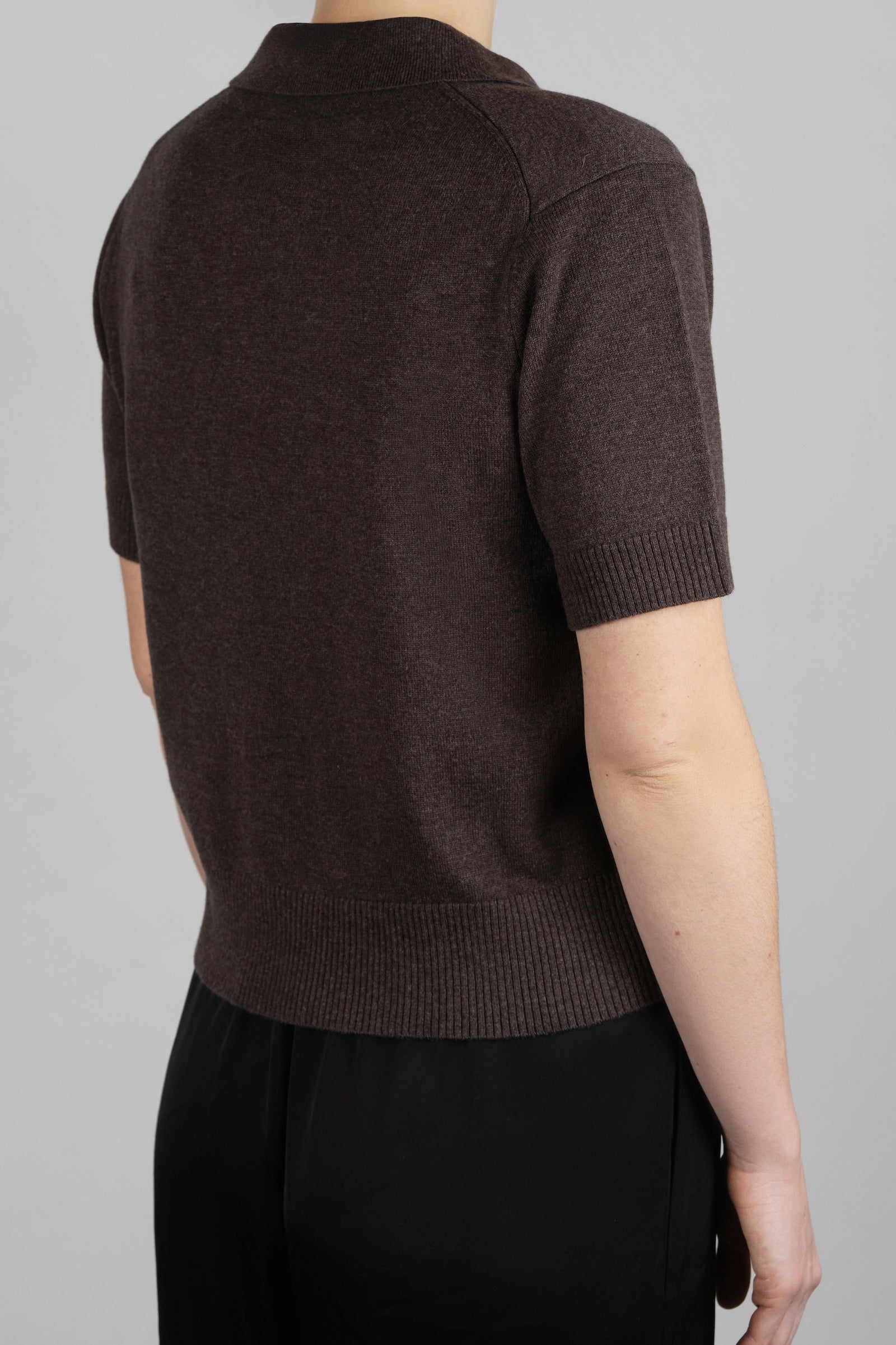 Person wearing a brown short-sleeve sweater against a gray background