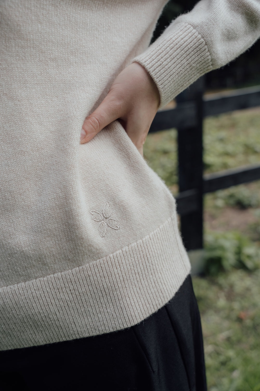 Close-up of the beige polo jumper's embroidered hem and ribbed cuff.